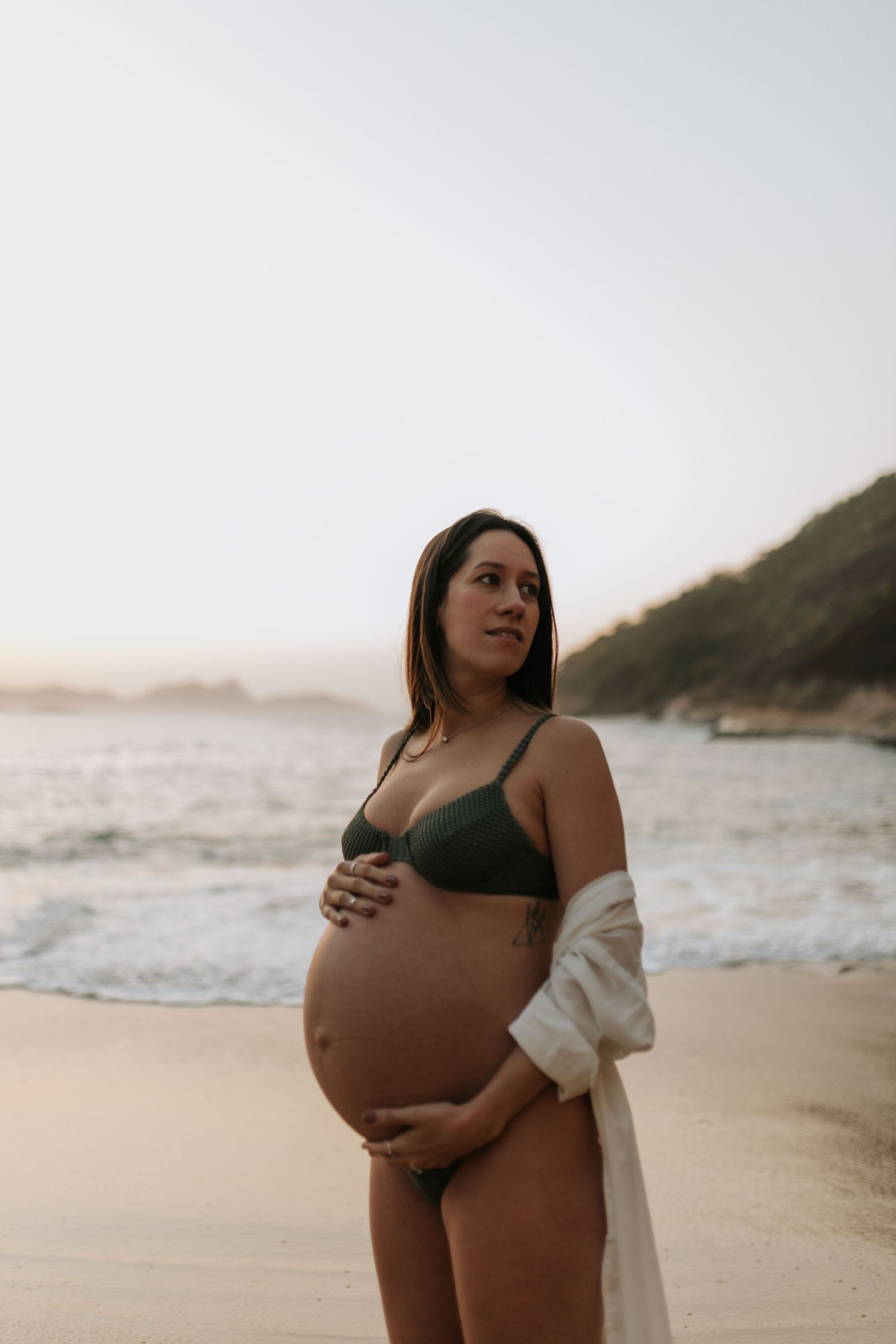 Maternity photo of expectant mother in black swimwear on beach at sunset.