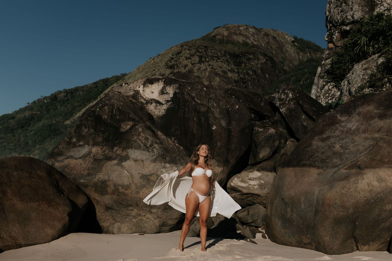 Woman in white dress posing on dramatic coastal rocks.