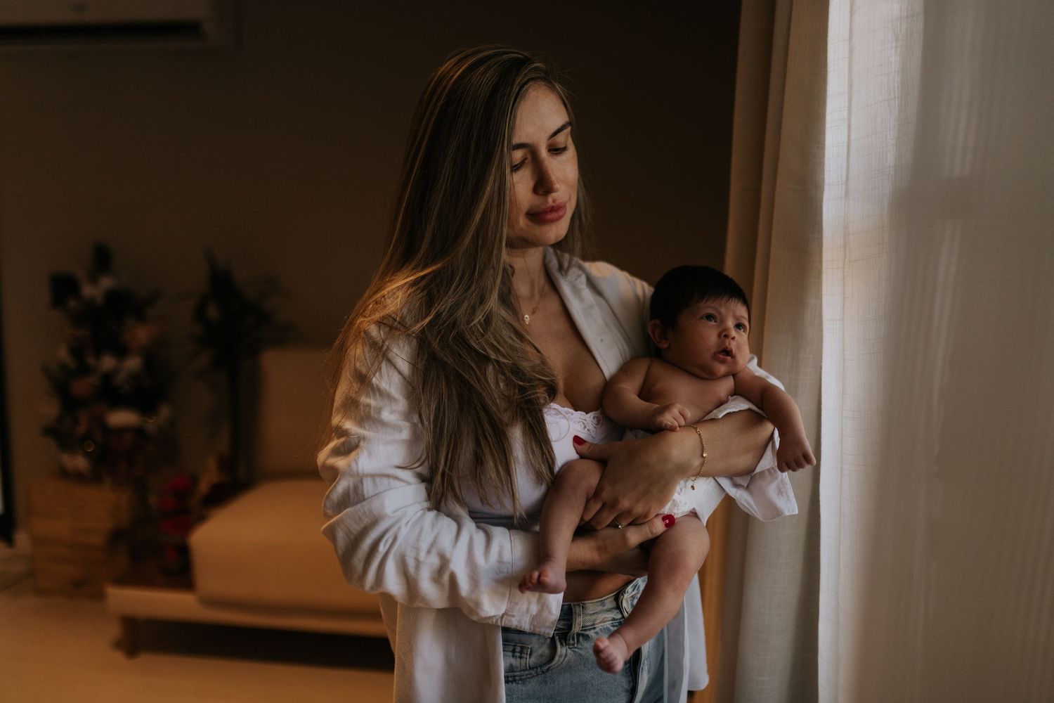 A cozy indoor scene showing a parent cradling a small infant near a window.