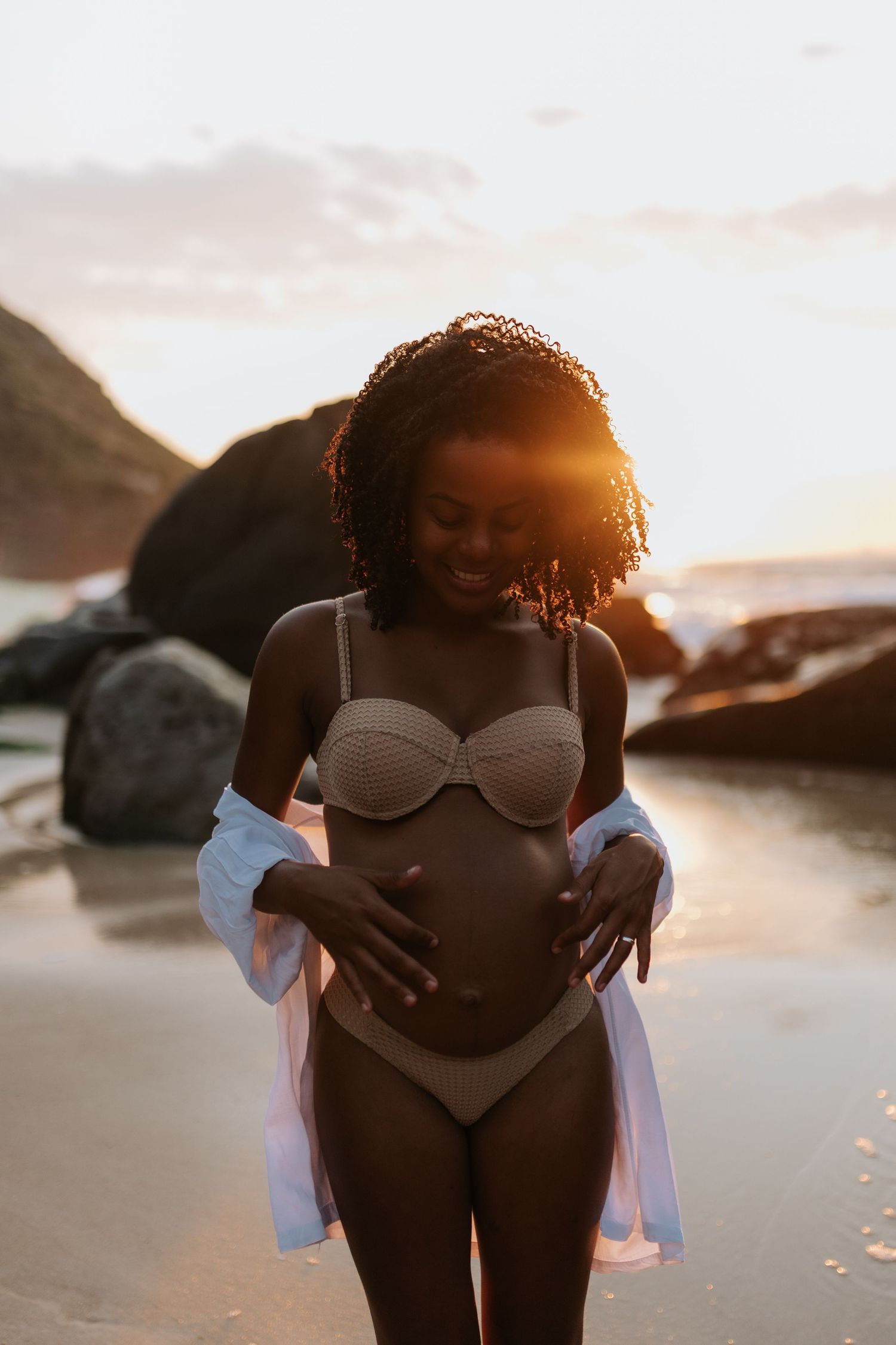 Intimate maternity photoshoot at sunset on a rocky beach with warm backlighting.