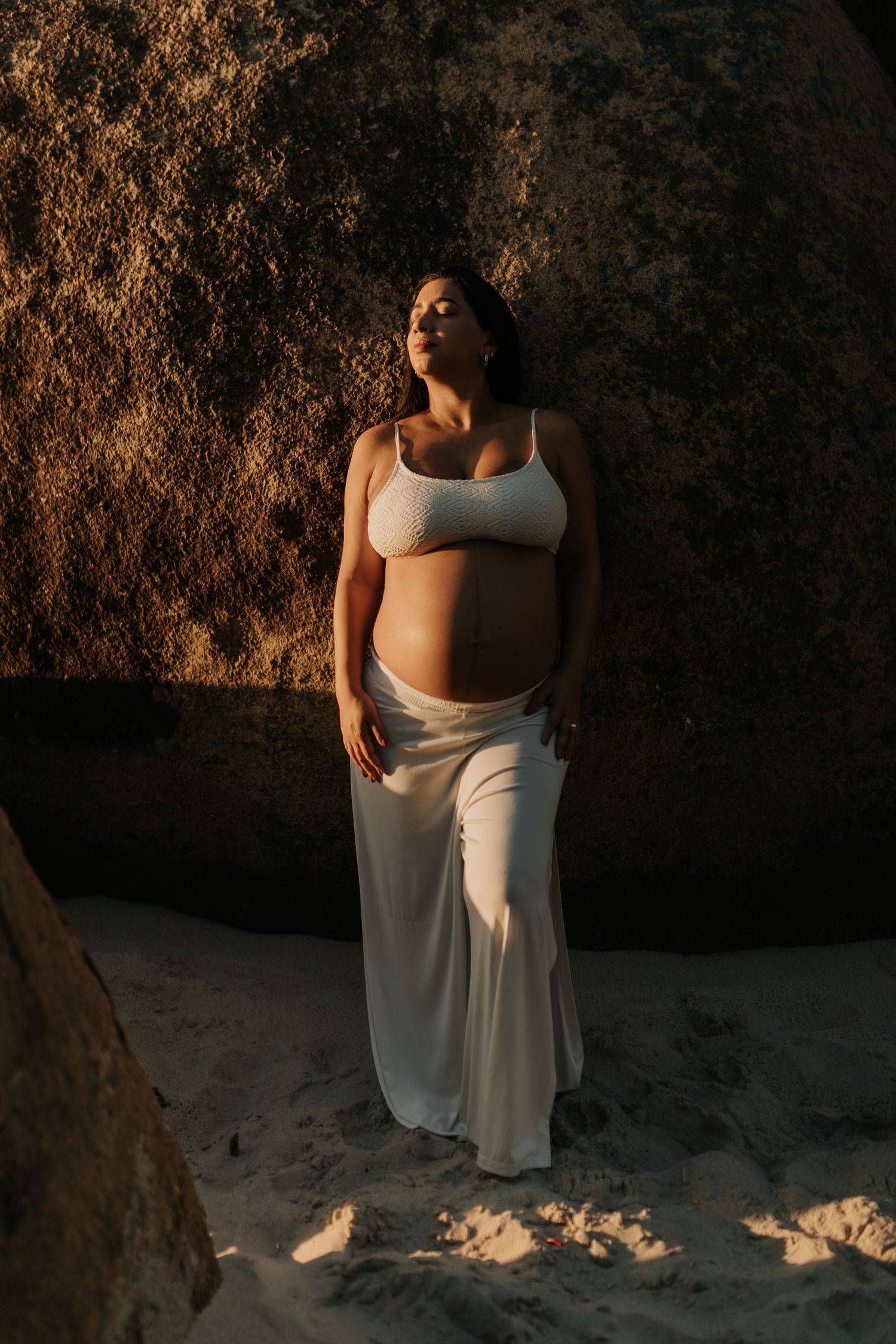 Artistic maternity portrait against a rocky backdrop in golden evening light.