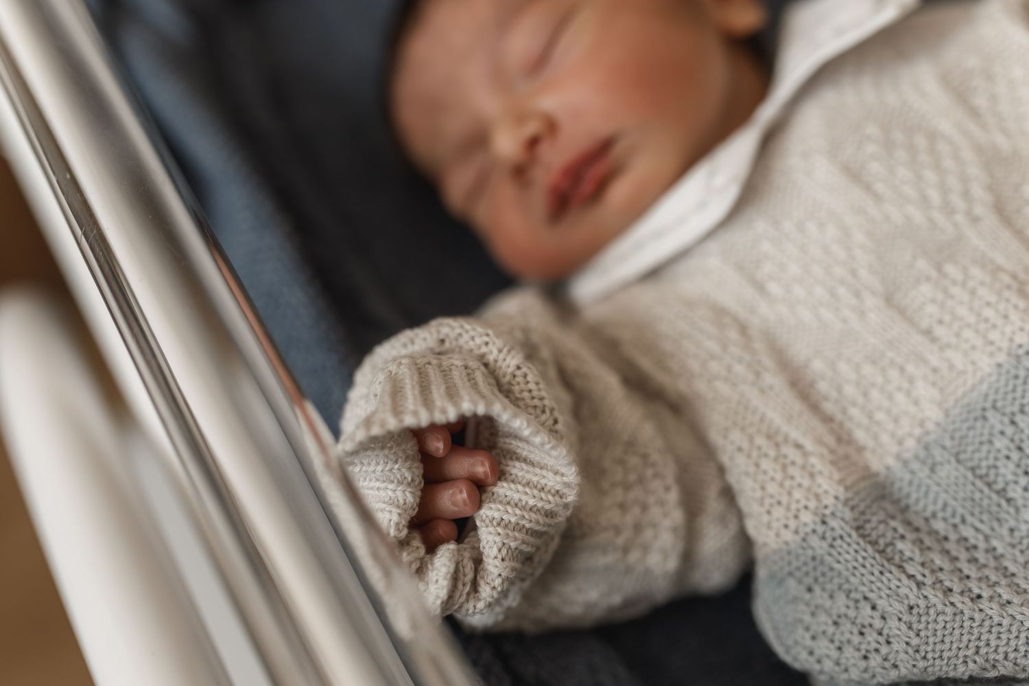 Close-up of a peaceful sleeping baby wrapped in white knitted blanket.