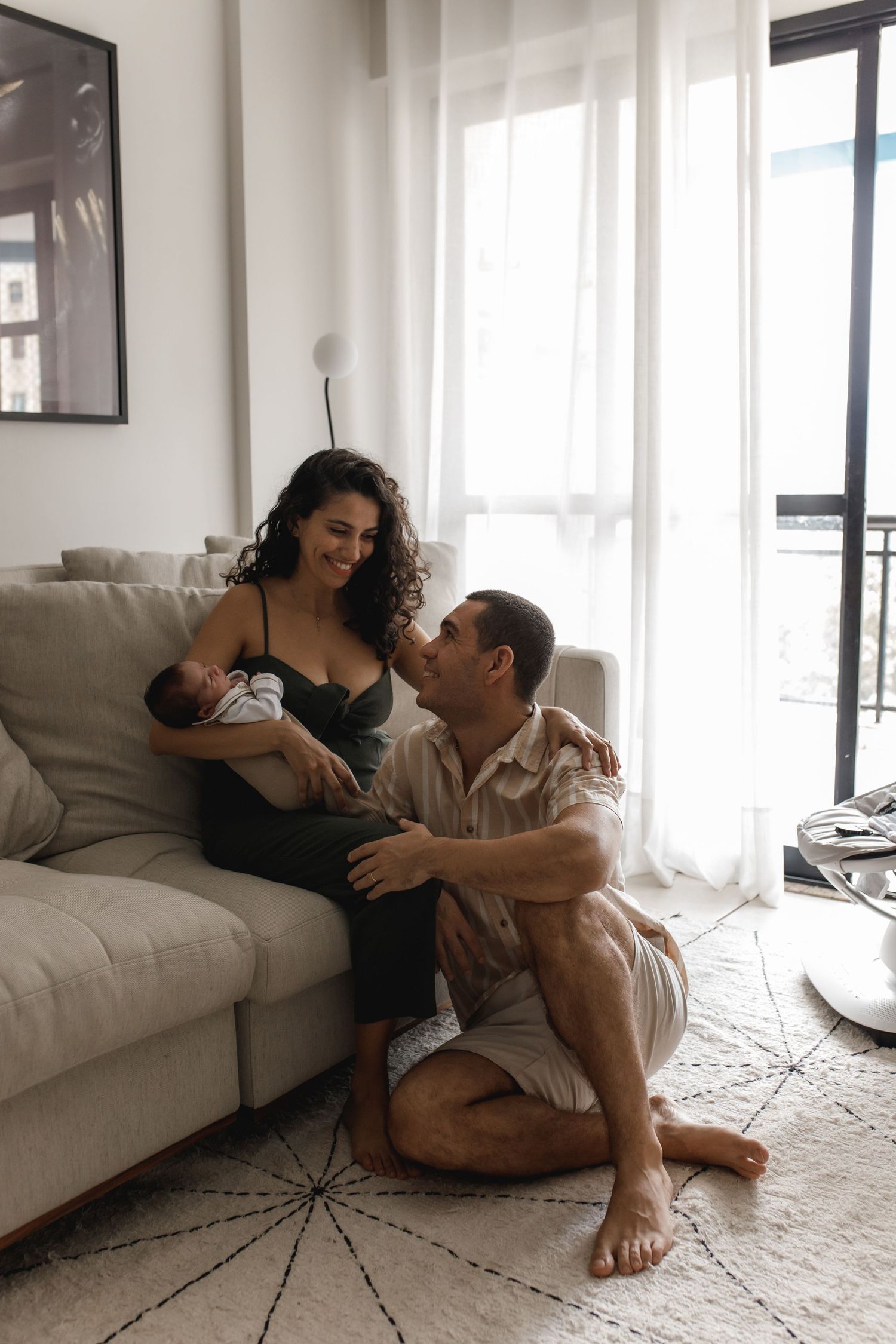 Family relaxing together on living room floor with natural lighting streaming through windows.