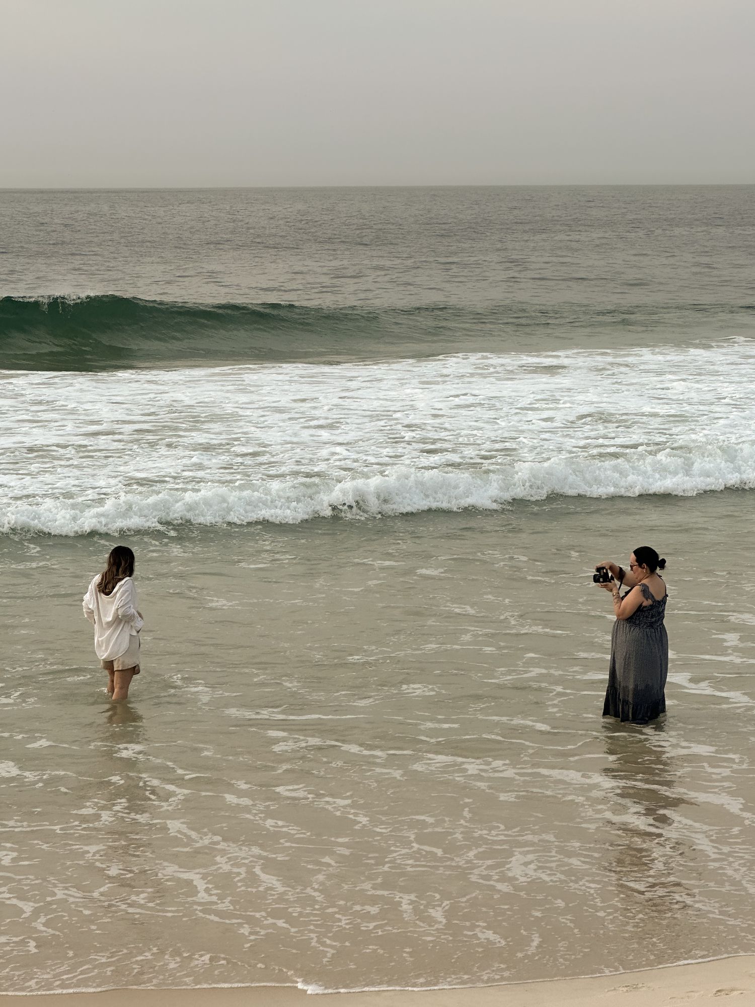 People standing in ocean waves during overcast beach photoshoot.
