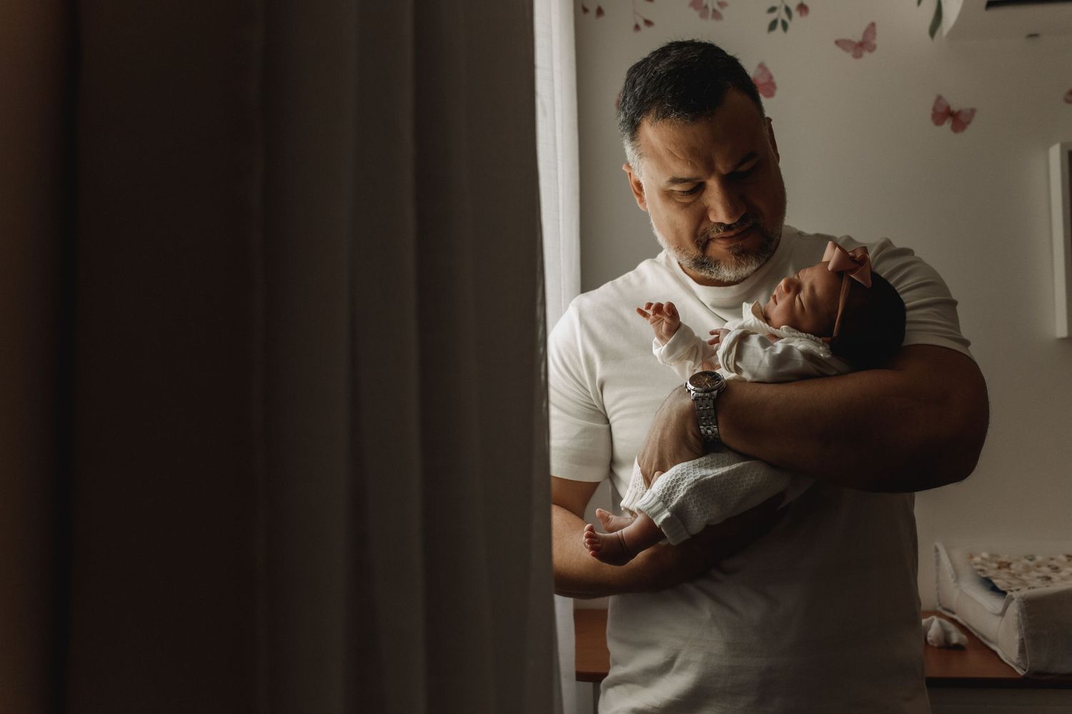 Parents sharing tender moment with newborn in natural window light.