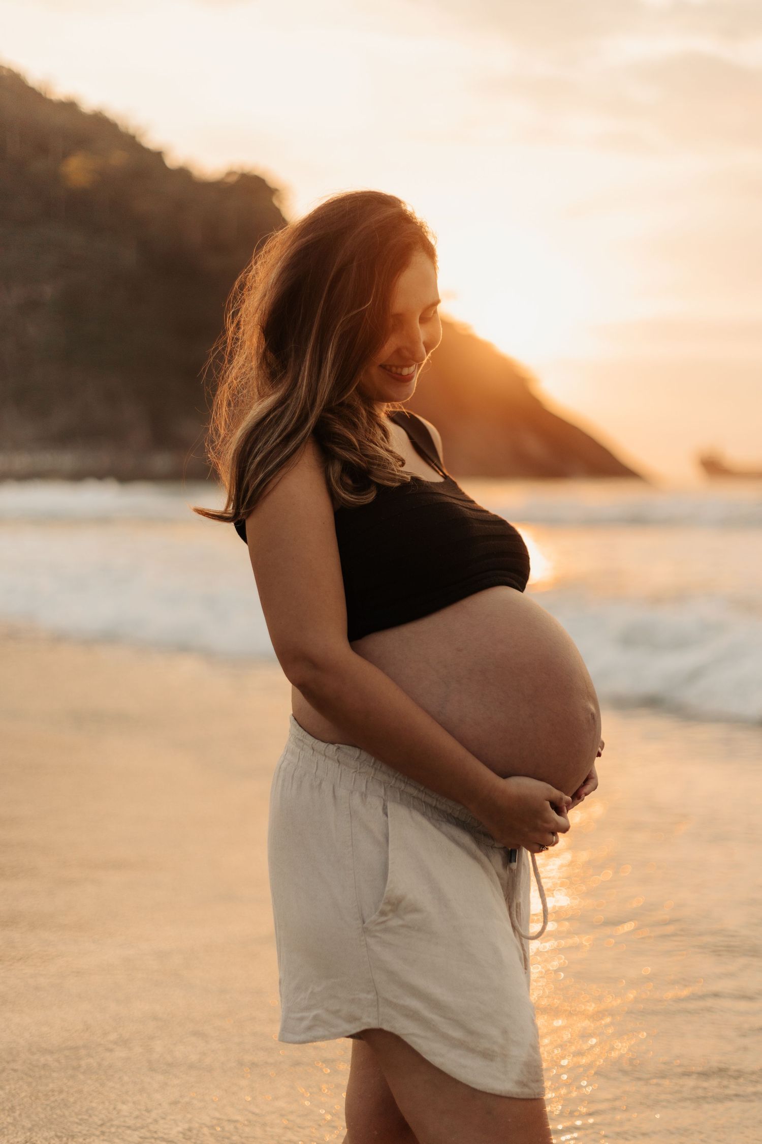 Maternity beach photoshoot during golden hour with ocean waves in the background.