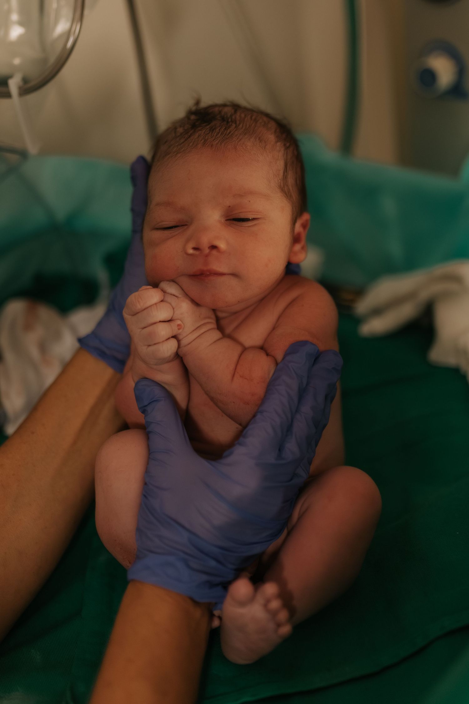 Newborn baby being examined by medical staff wearing purple gloves.