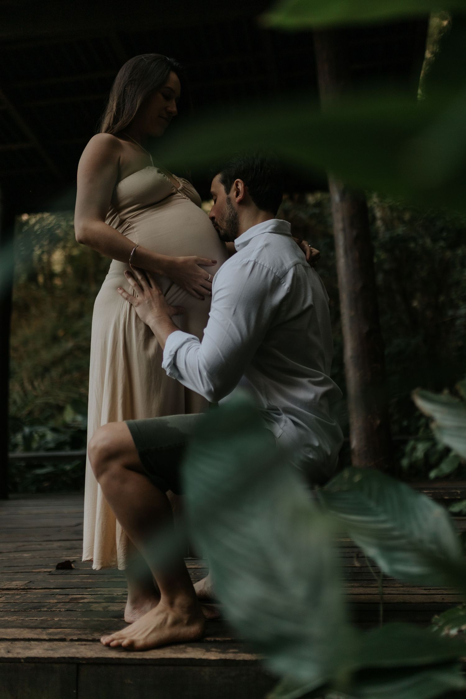 Intimate maternity photo session on wooden deck in moody lighting.