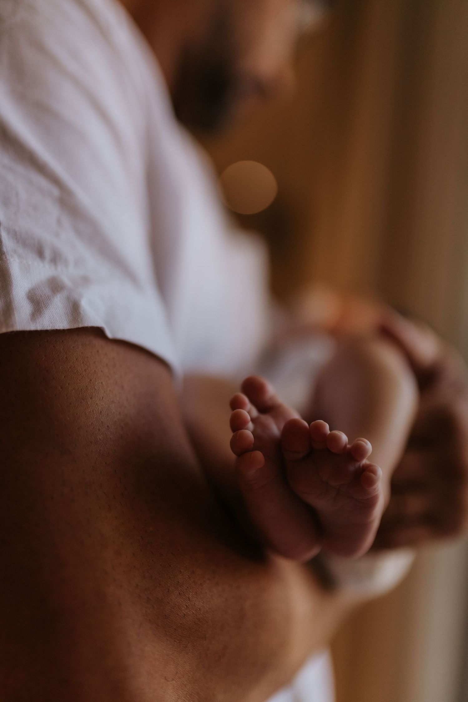Close-up shot of tiny baby feet resting against someone wearing a white shirt.