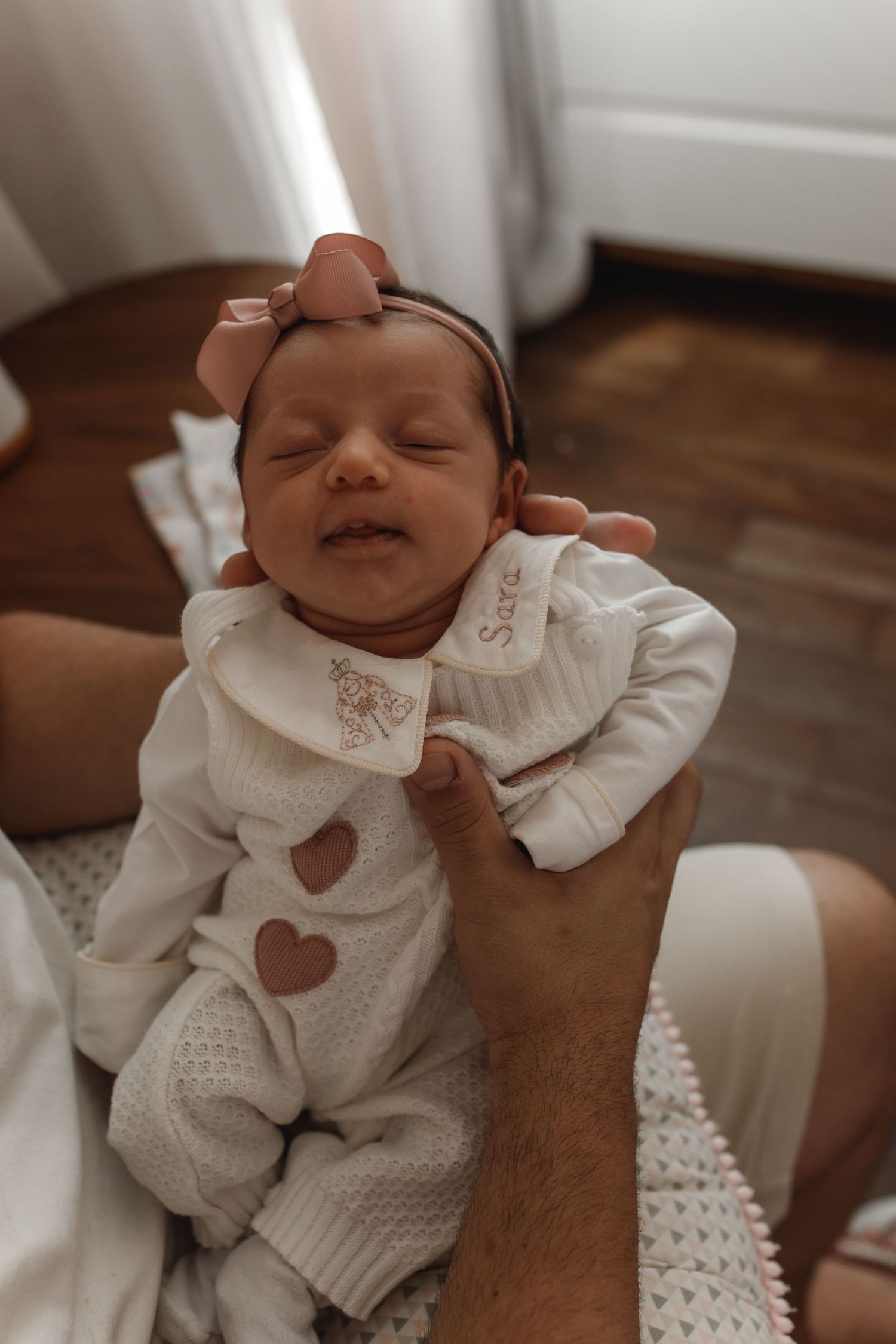 Baby wearing white knit outfit with heart design lying on brown surface.