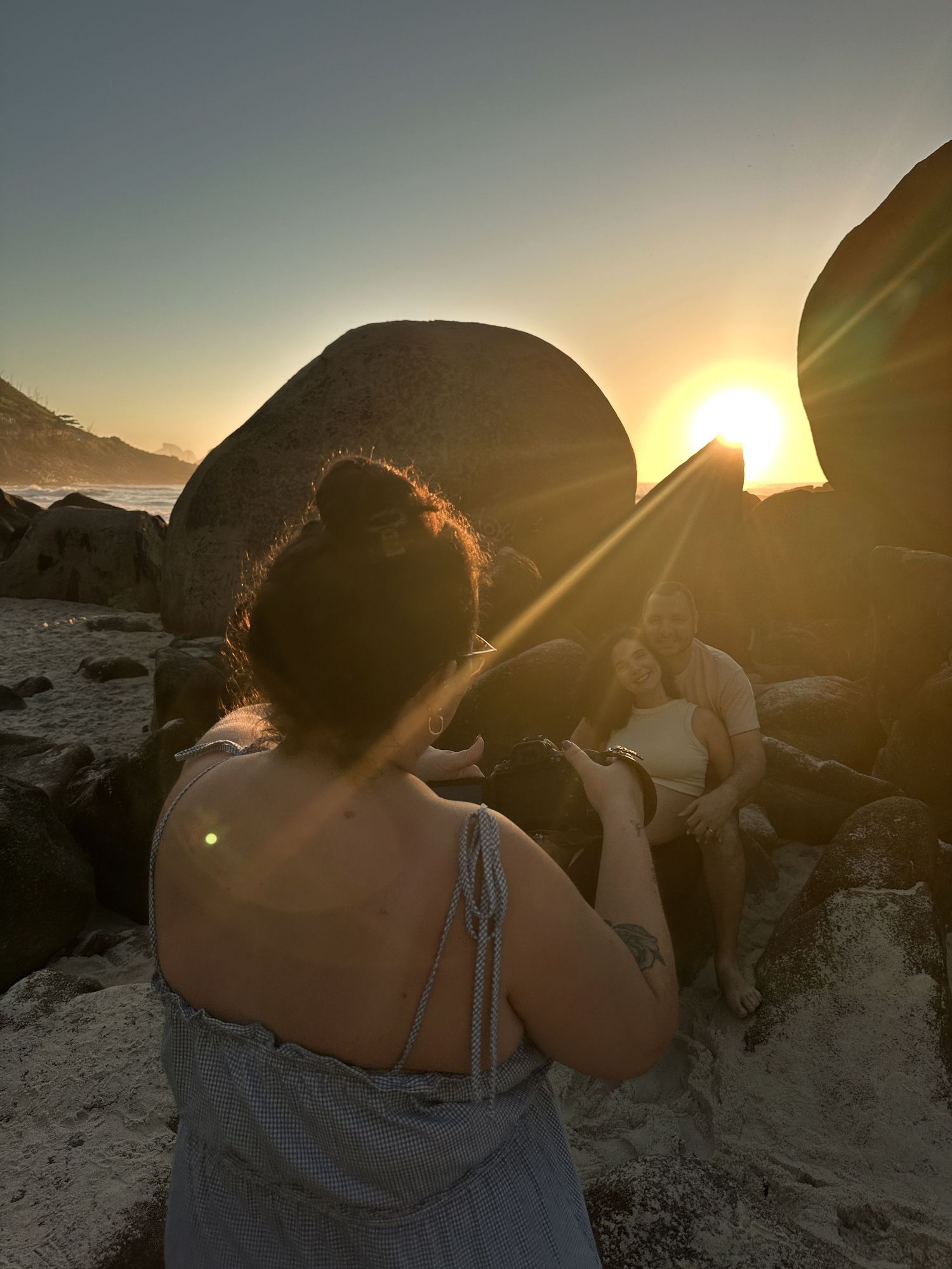 Group watching sunset between large rock formations on beach.