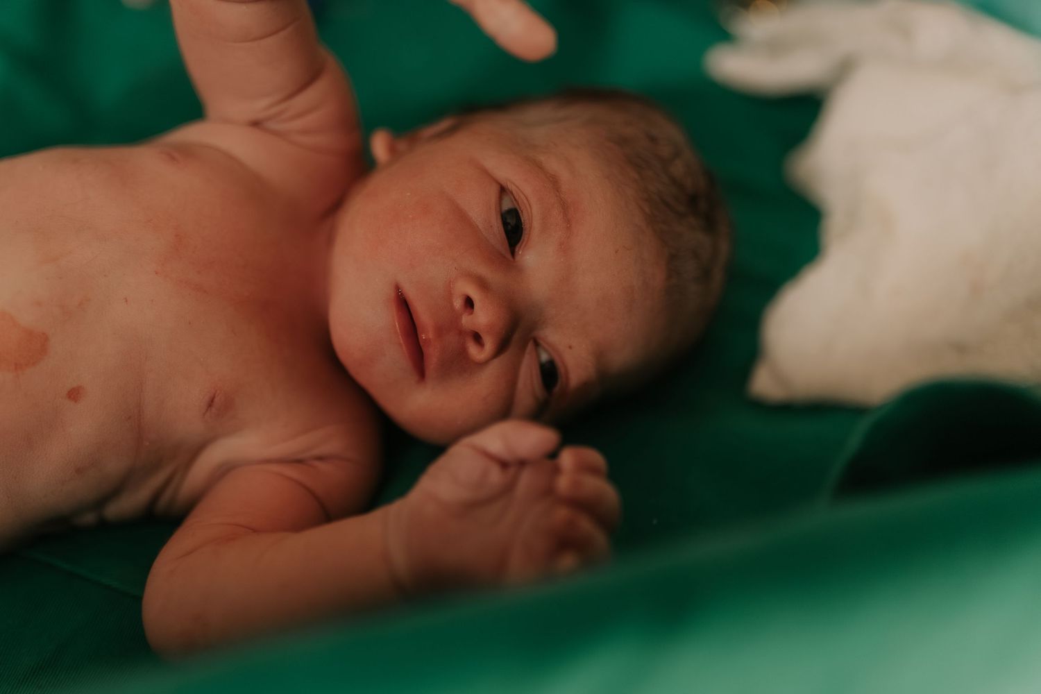 Newborn baby lying on green medical sheets during post-birth examination.