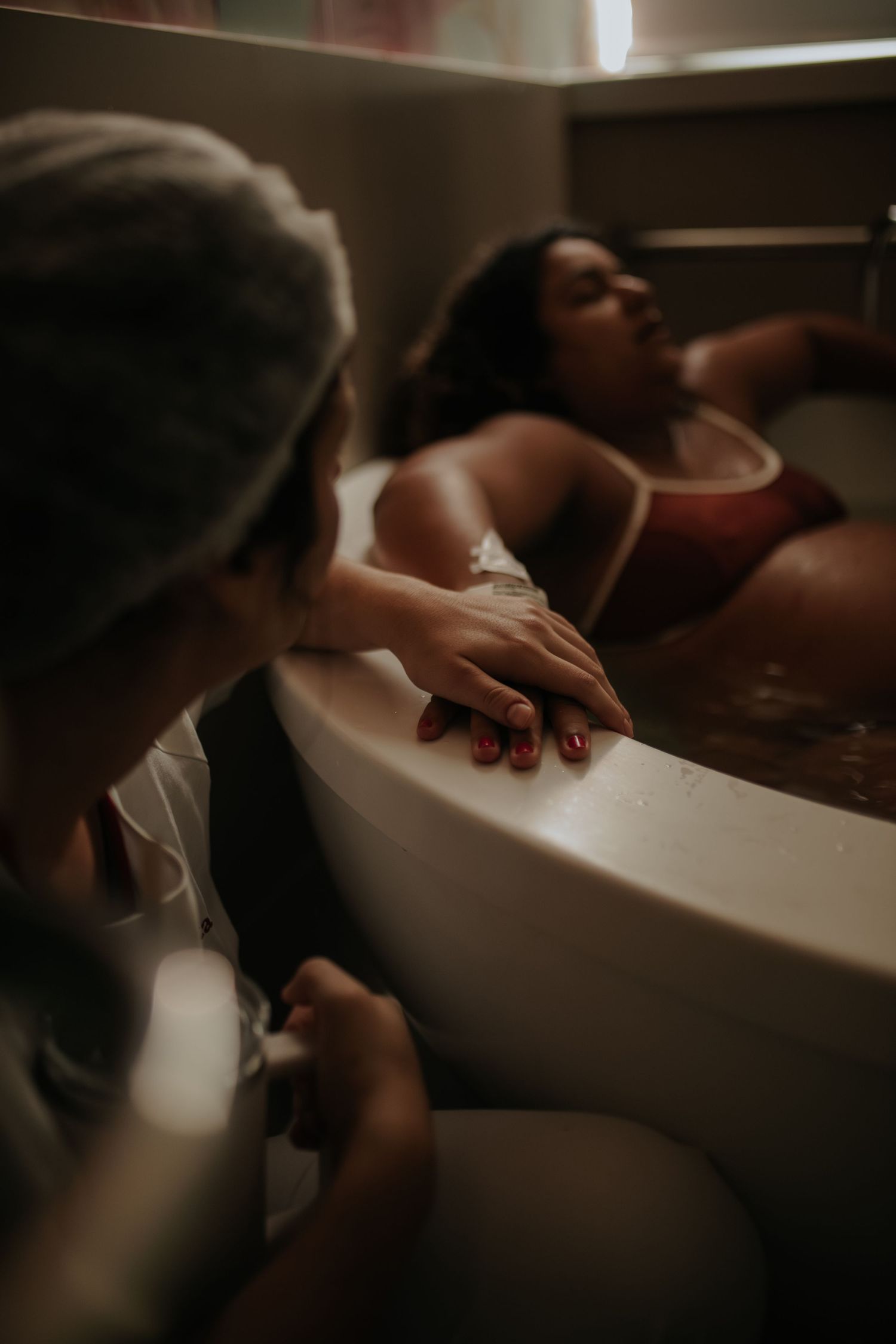Artistic maternity photography session in a bathtub with moody lighting.