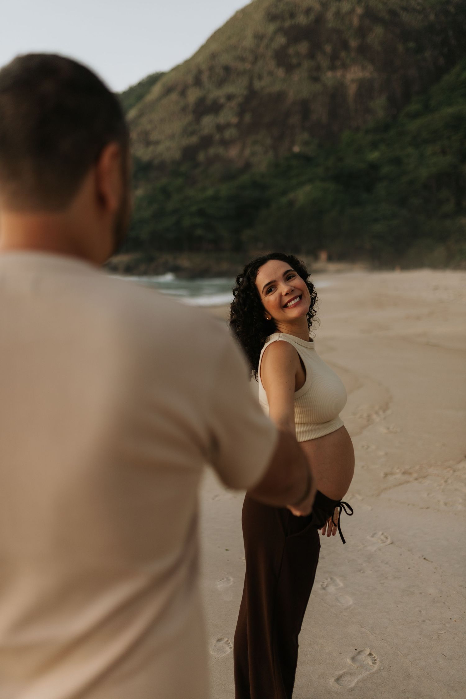 Candid beach maternity photoshoot with mountains and coastline in the background.
