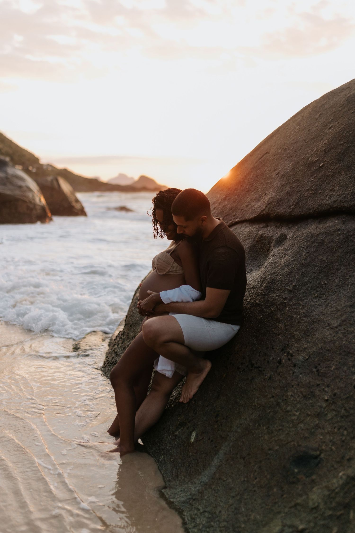 Romantic maternity photos captured against ocean backdrop during golden hour.
