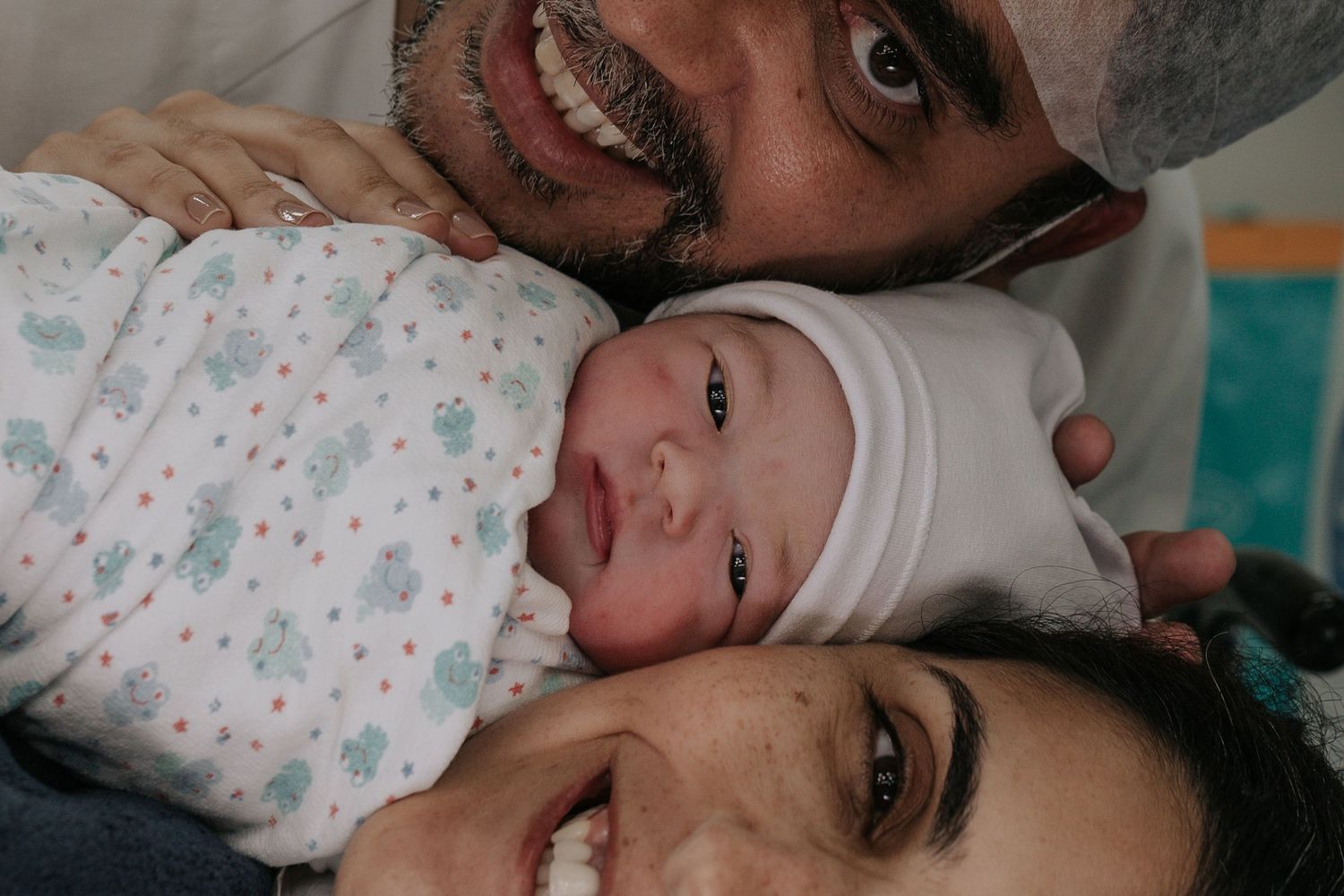 A newborn baby wrapped in a white and floral patterned blanket lies peacefully in a hospital setting.