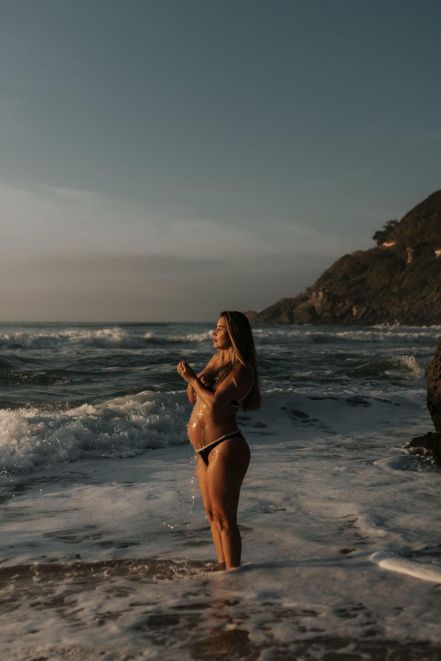 Person in swimwear standing in ocean waves during moody coastal photoshoot.