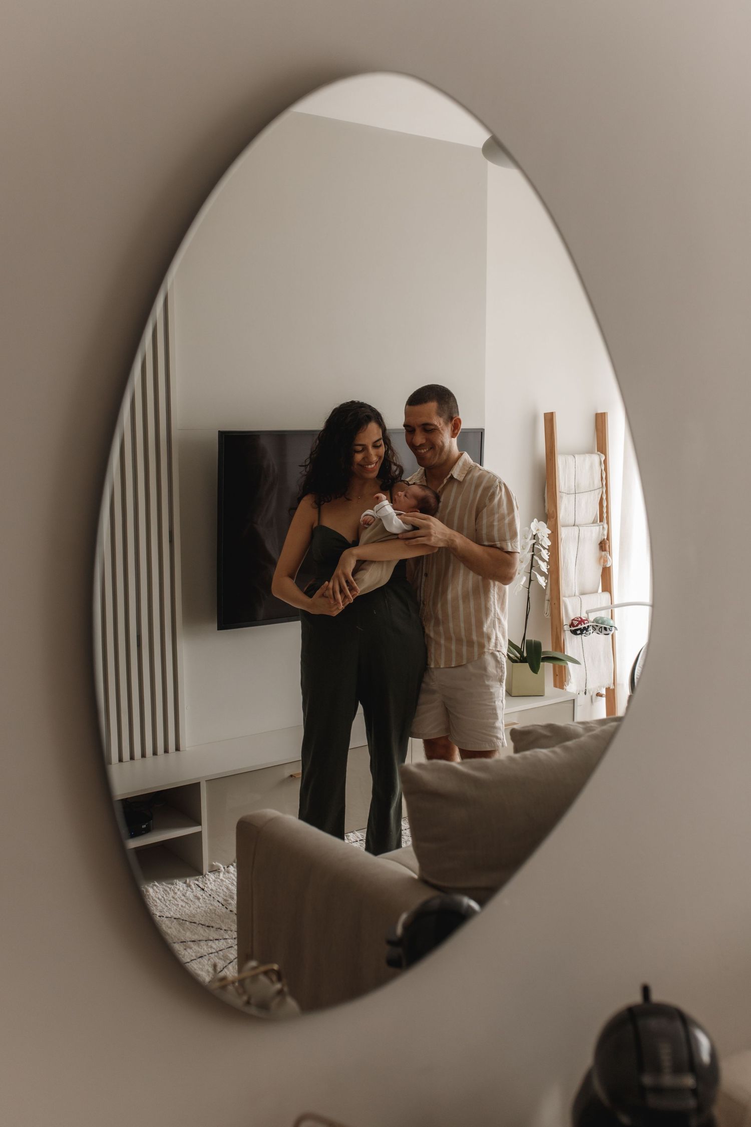 Family lifestyle moments reflected in round mirror against neutral wall.