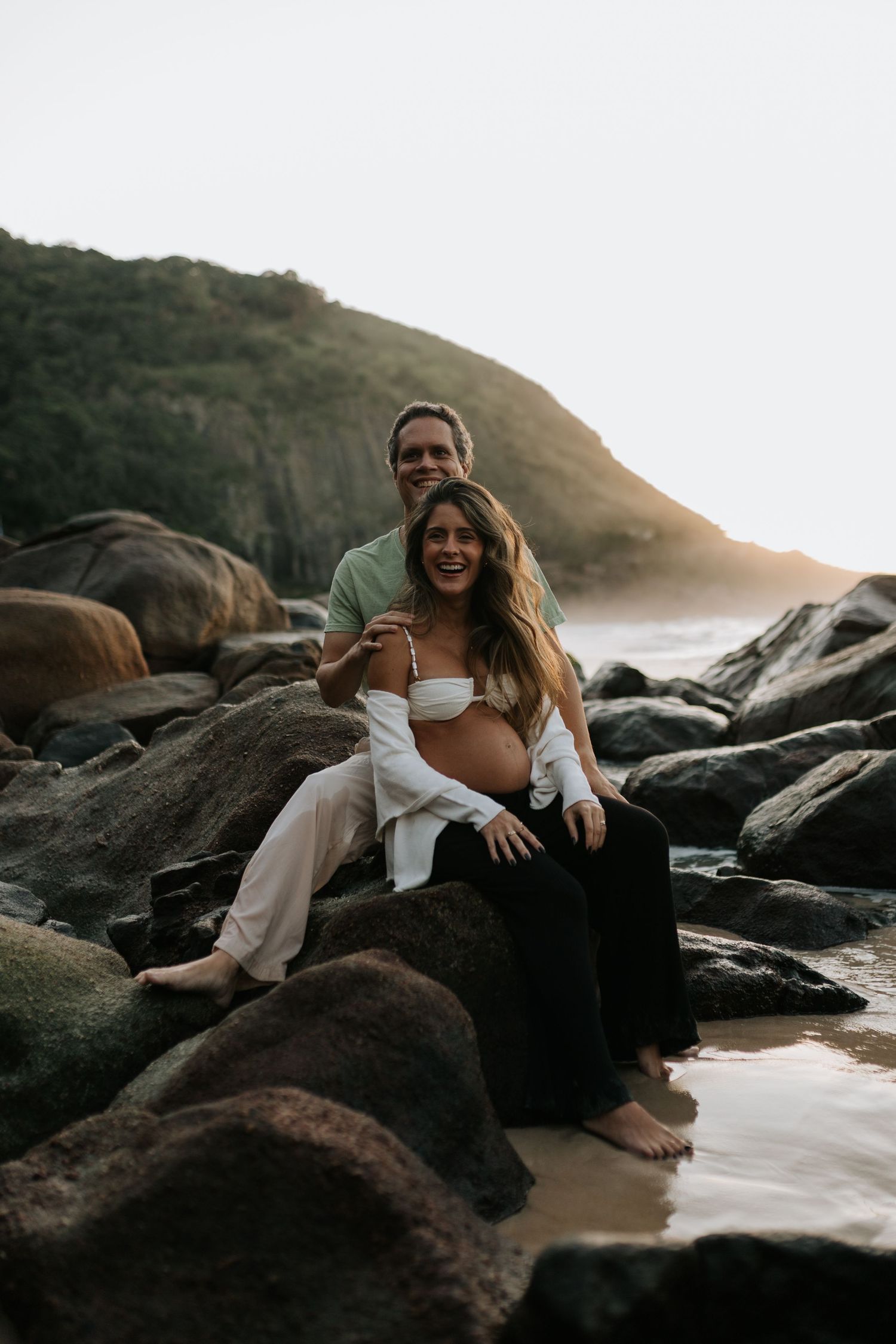 Couple relaxing on rocky beach formation during sunset.