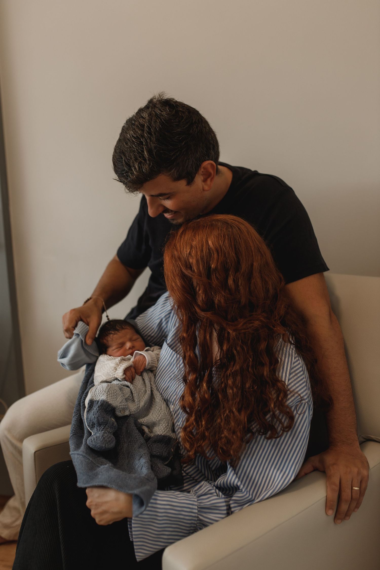 Family relaxing on white furniture while bonding with their newborn baby.
