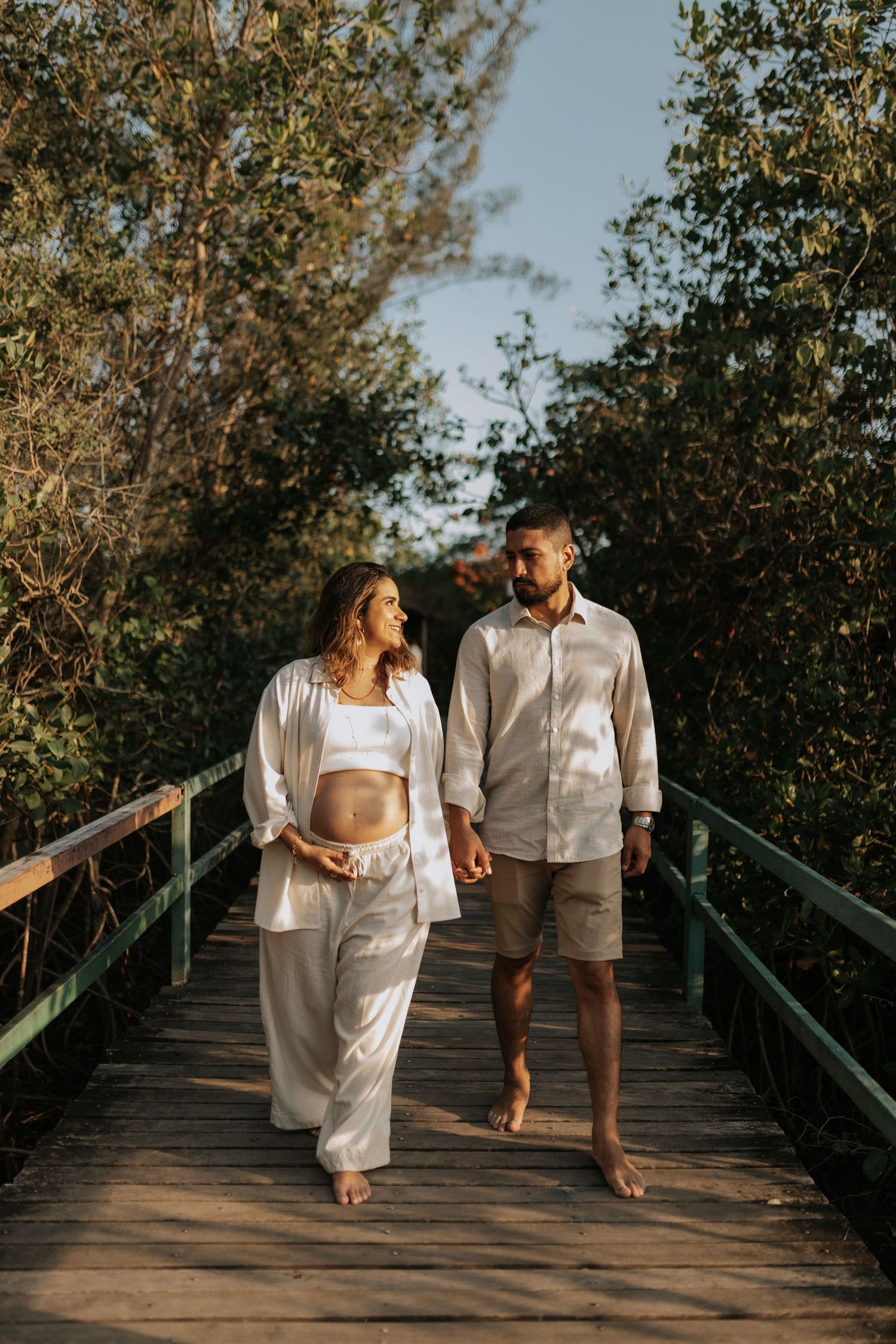 Couple strolling barefoot together on a wooden boardwalk surrounded by lush greenery.