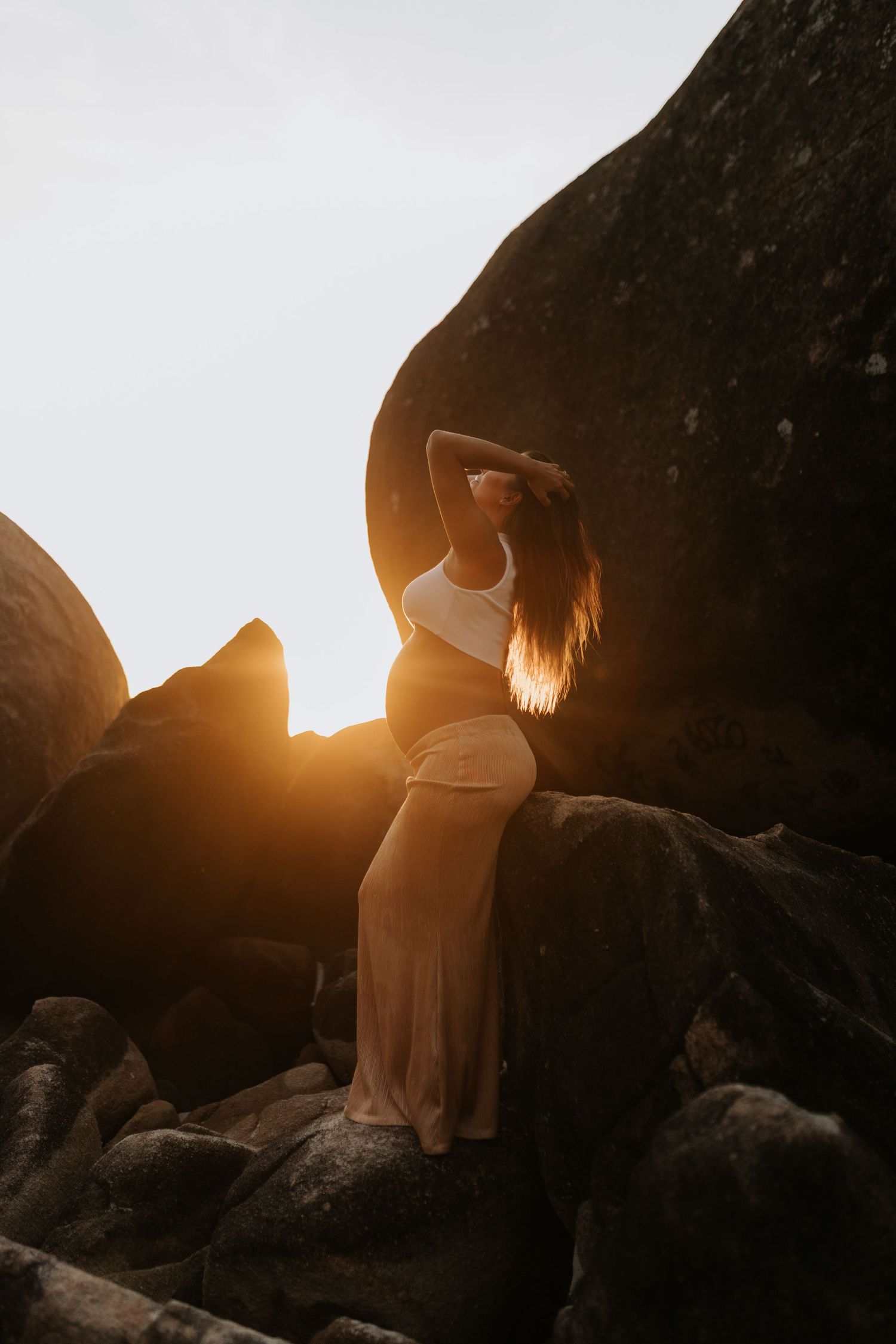 Silhouette of a pregnant woman against a golden sunset between rocky formations on the beach.