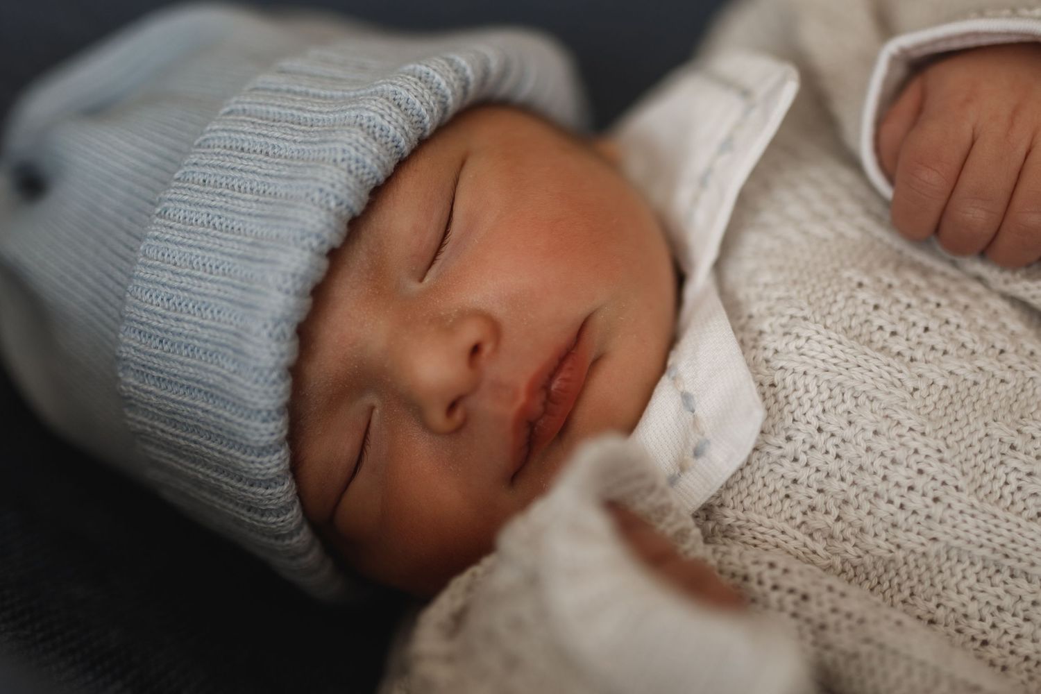 Sleeping infant wearing a soft gray knit outfit resting on white bedding.