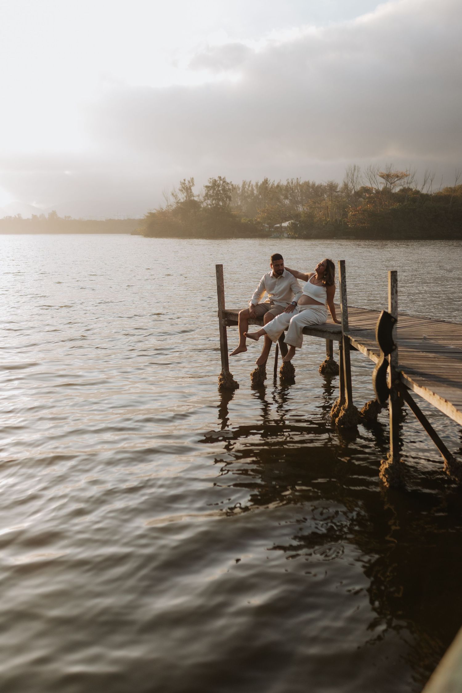 Couple posing playfully on a wooden dock over calm waters at dusk.