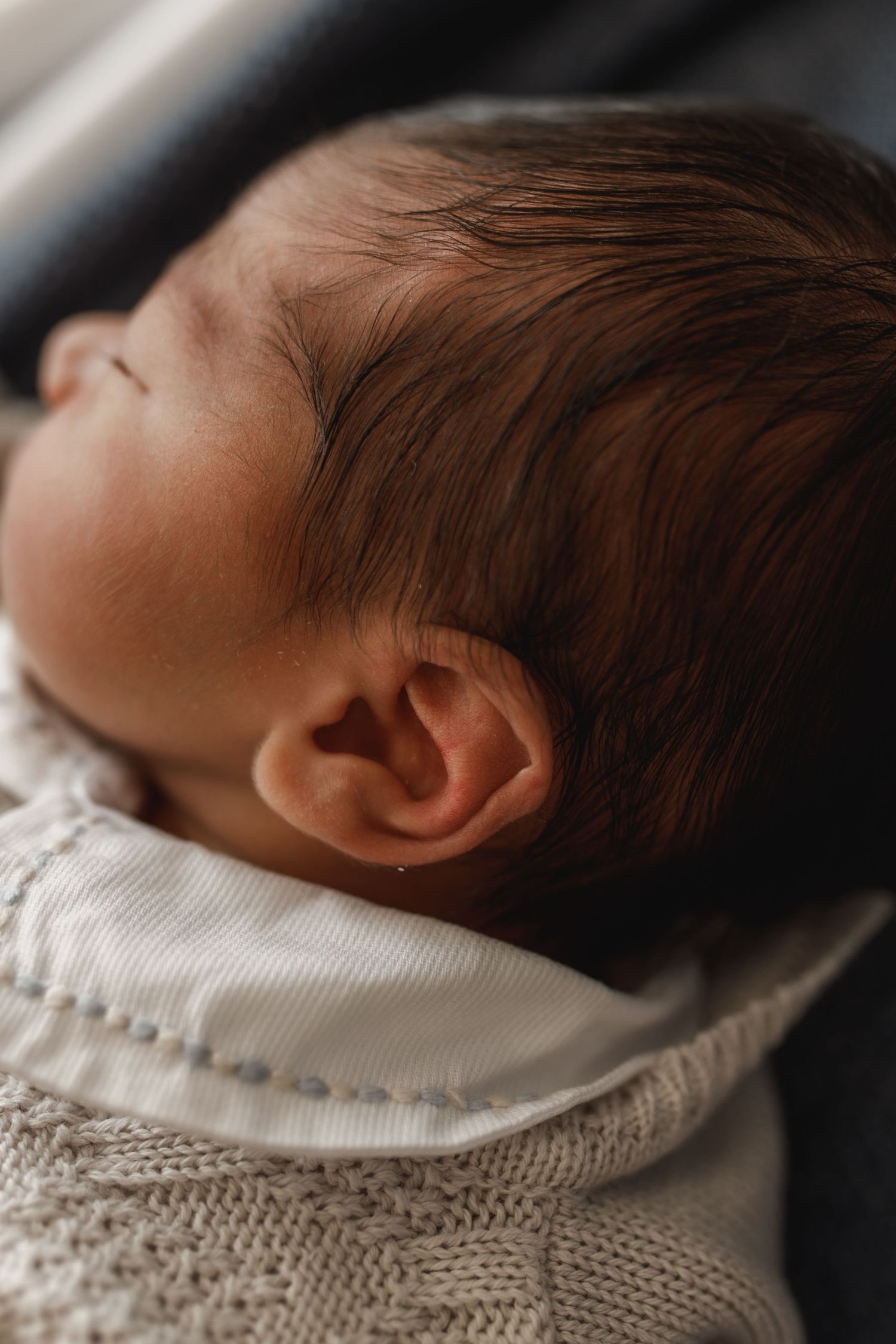 Side profile of sleeping newborn wrapped in white knitted fabric.