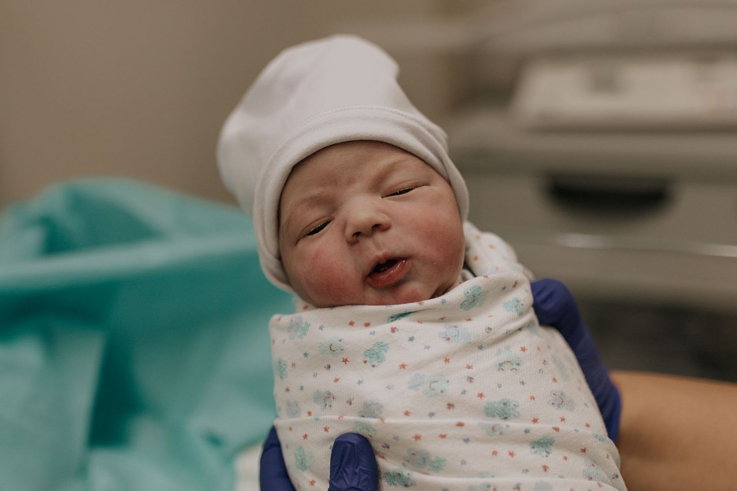 Newborn baby wrapped in a patterned blanket resting in a hospital bassinet.