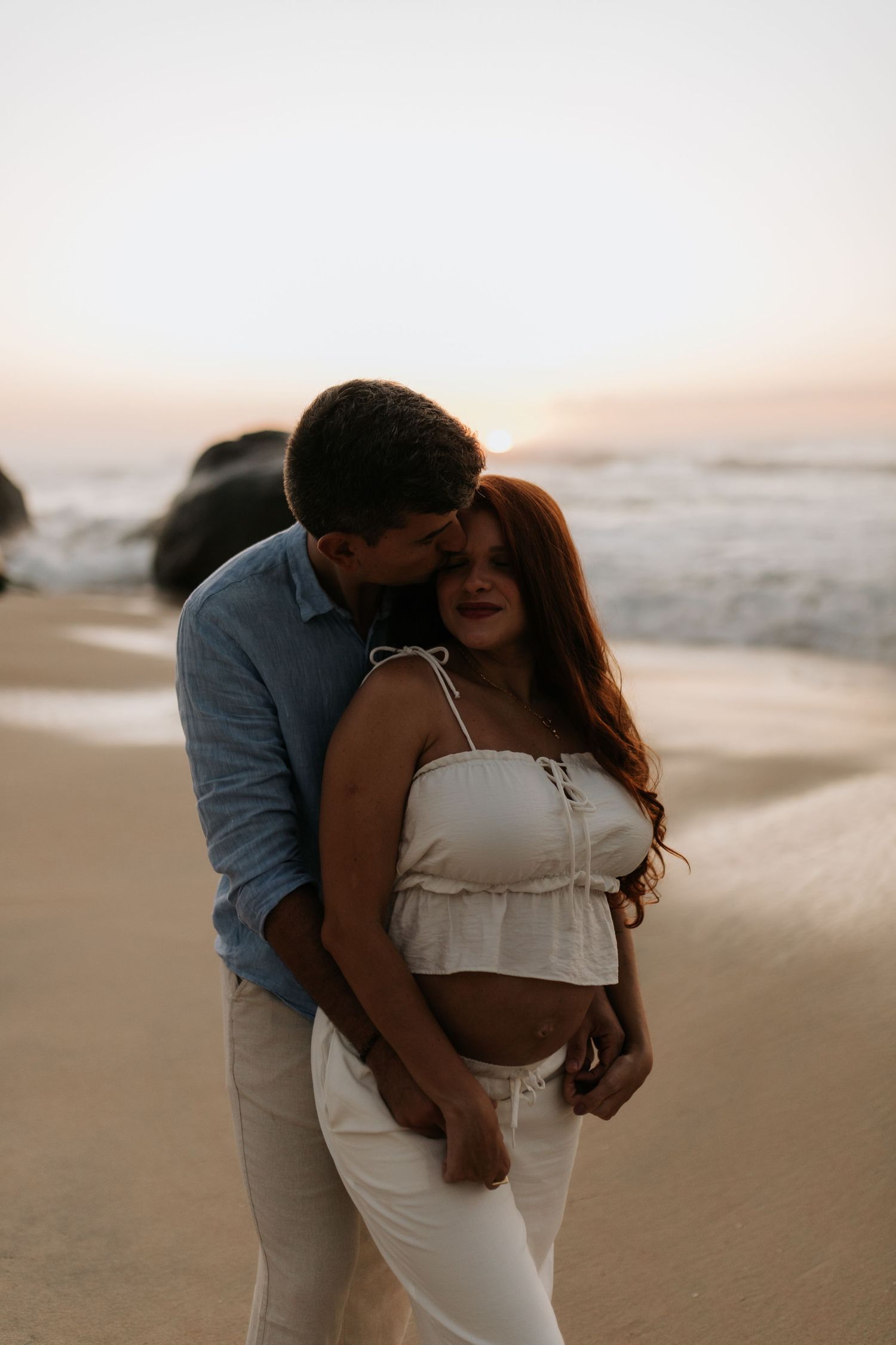 Intimate beach maternity portrait with couple embracing during sunset.