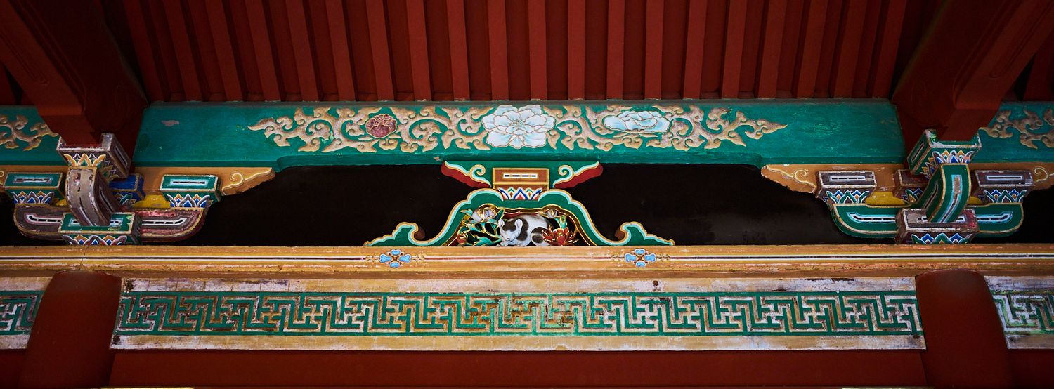 Ornate Japanese shrine architecture with a carved green and gold beam, decorative painted patterns, and red wooden eaves overhead.