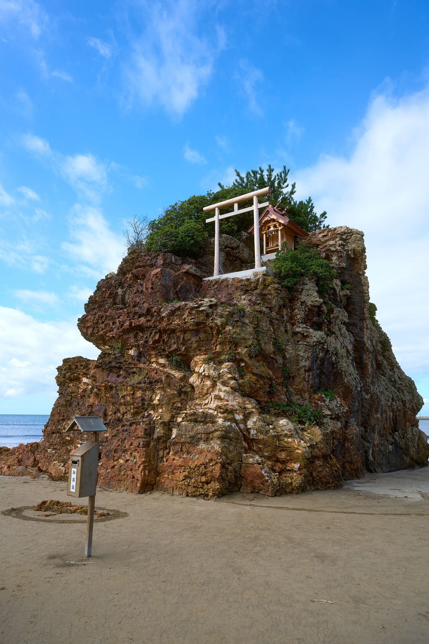 Rocky outcrop on a beach with traditional Japanese torii gates perched on top.