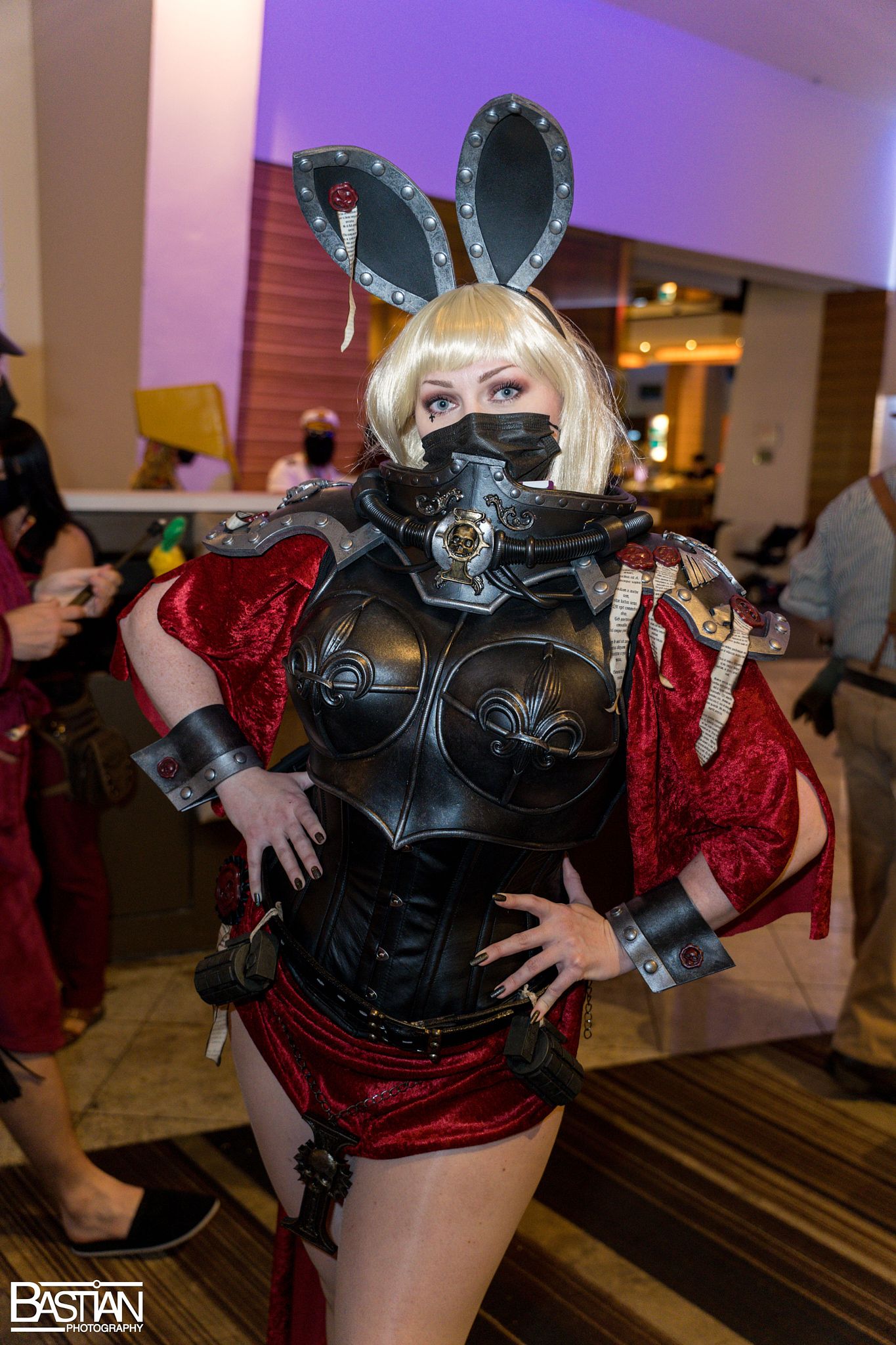 Cosplayer in black and red costume with bunny ears performing at an indoor event.