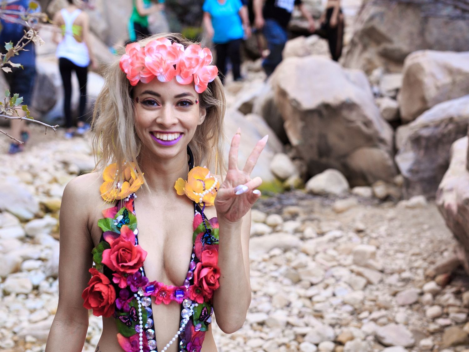Woman in floral swimsuit posing by rocky beach setting.