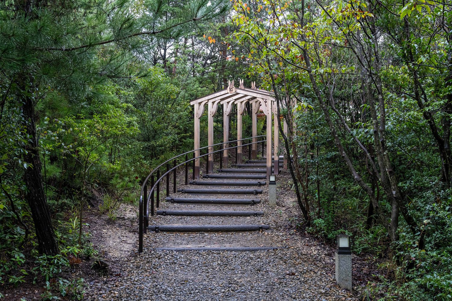 Stone steps wind through a lush green forest path with wooden railings and pergolas.