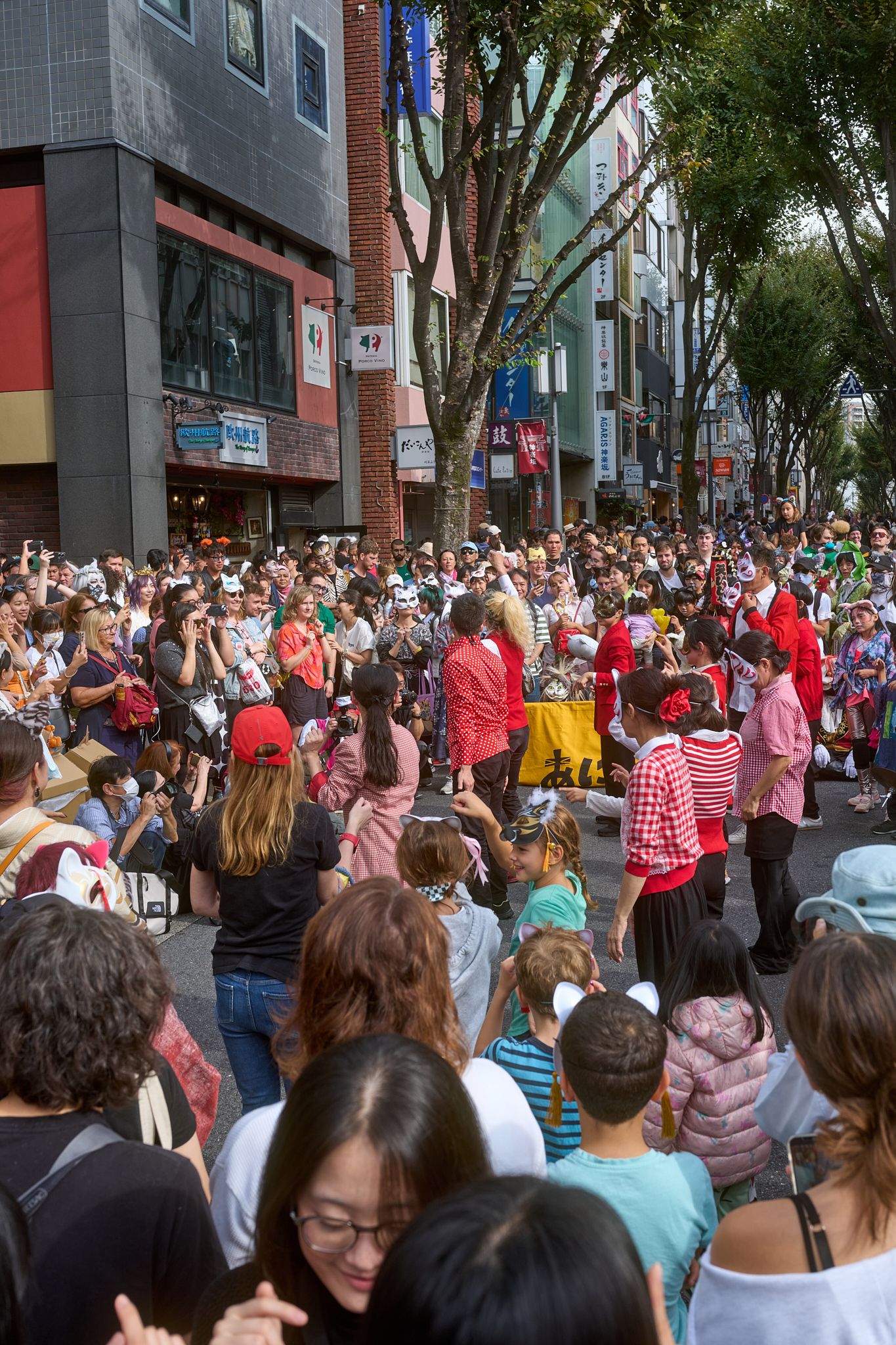 Large crowd gathered on a city street lined with trees and modern buildings.