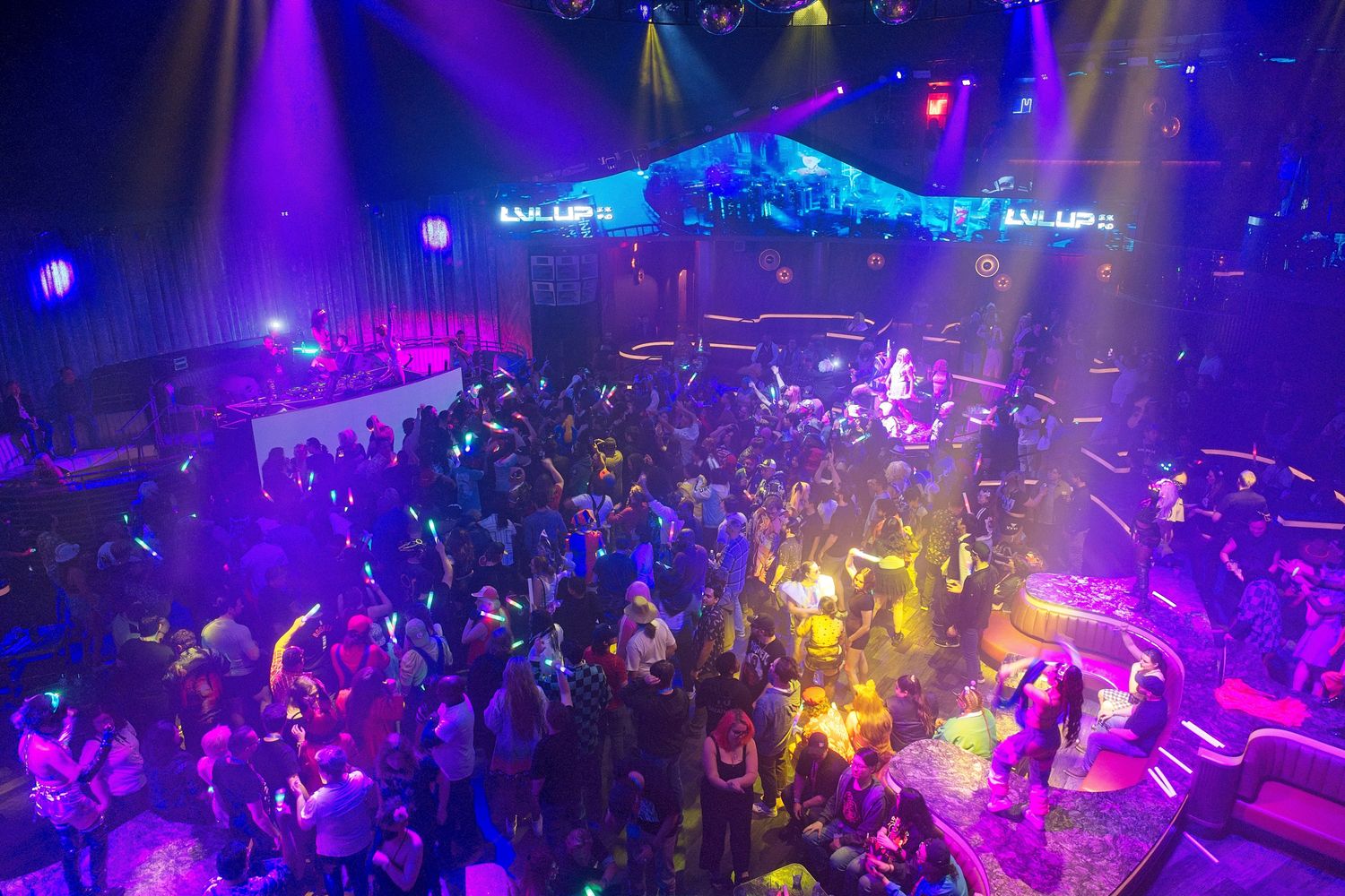 Nightclub interior with purple and yellow lighting effects illuminating a crowded dance floor.
