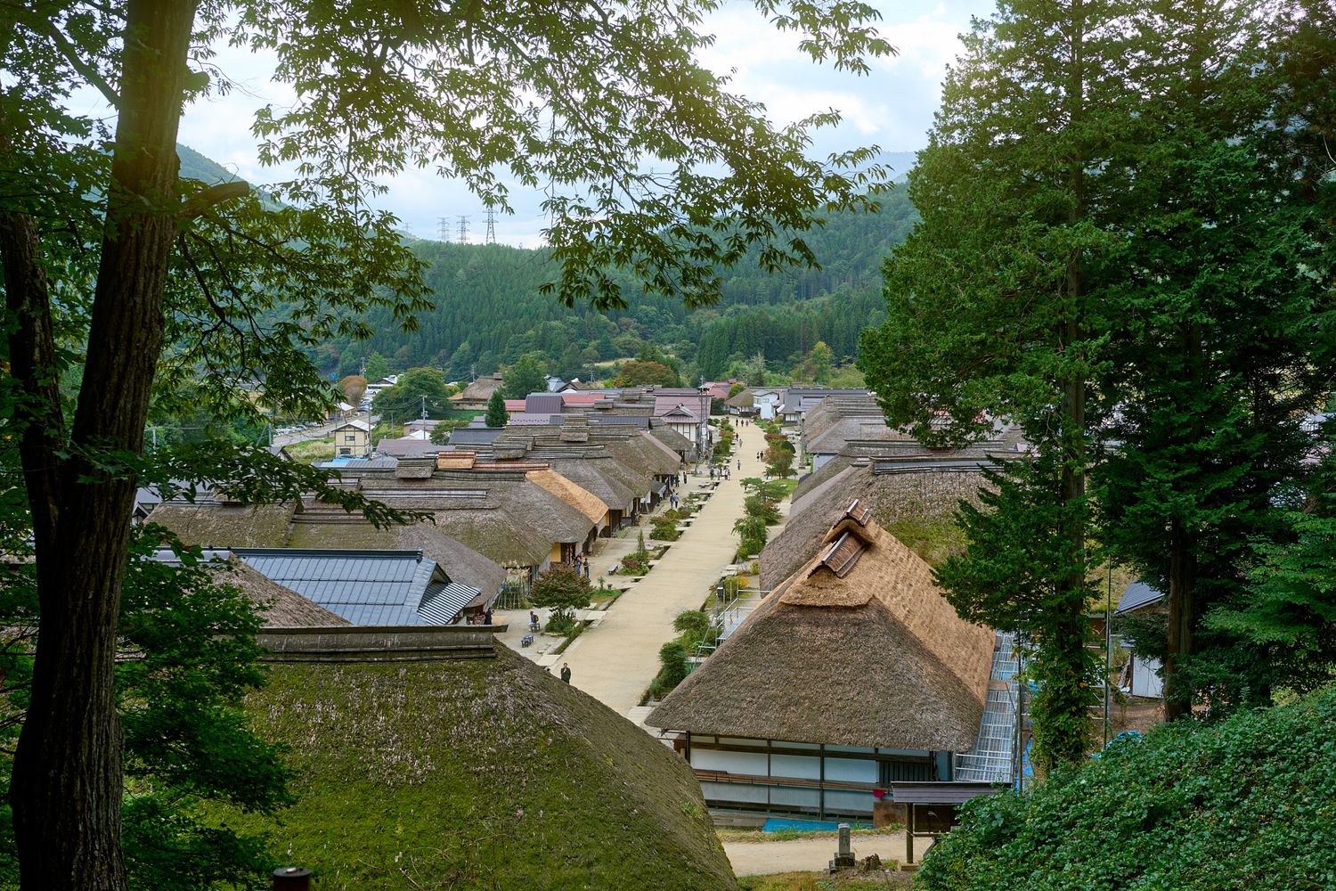 Panoramic view of a traditional Japanese village with tiled roofs nestled among green hills.