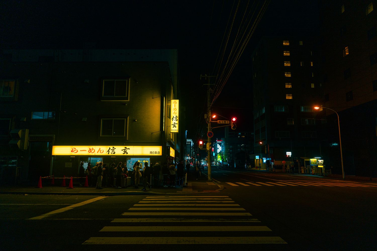 Dark urban street scene at night with distant traffic lights and building silhouettes.