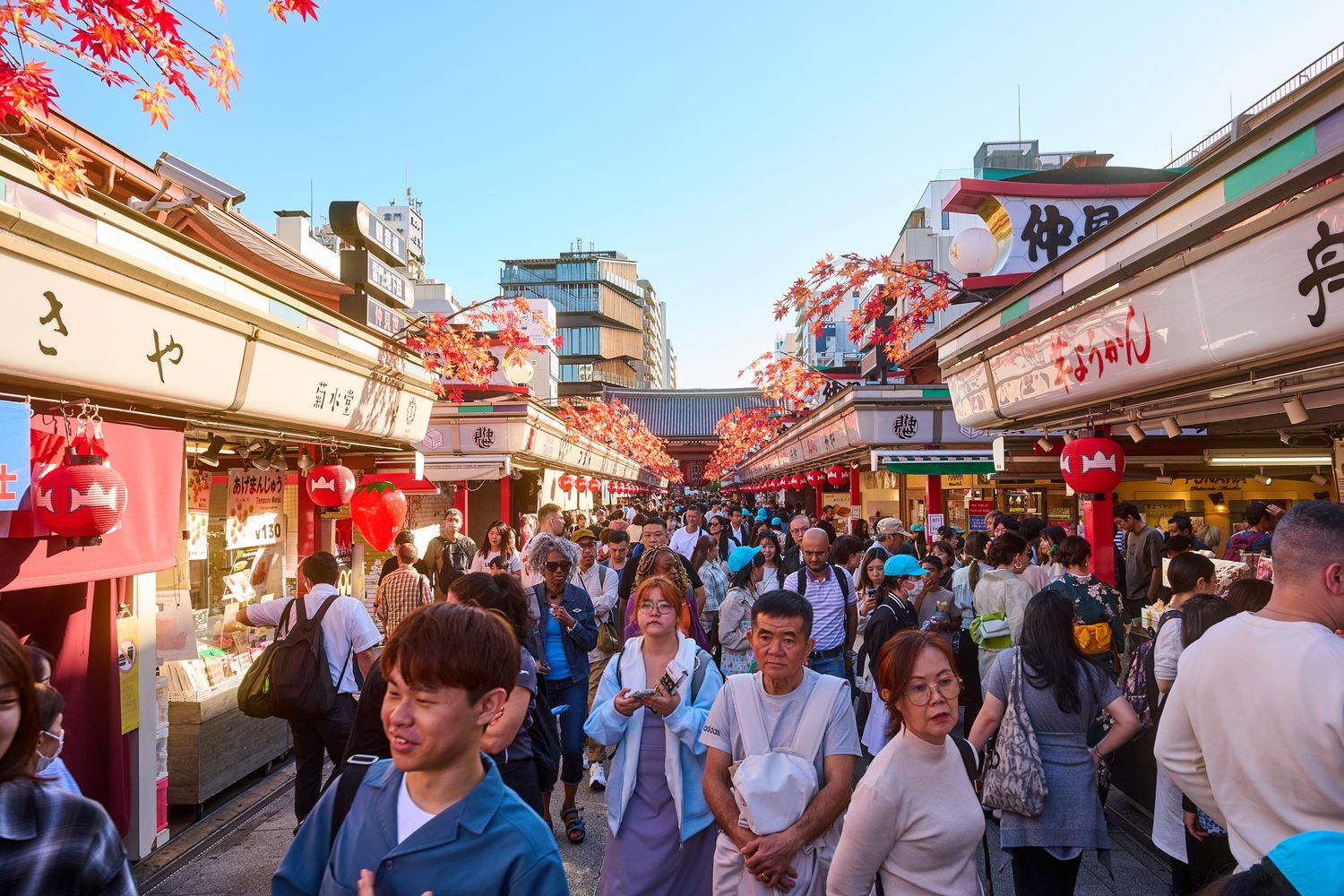 Crowded outdoor market street with red lanterns and vendor stalls during daytime.