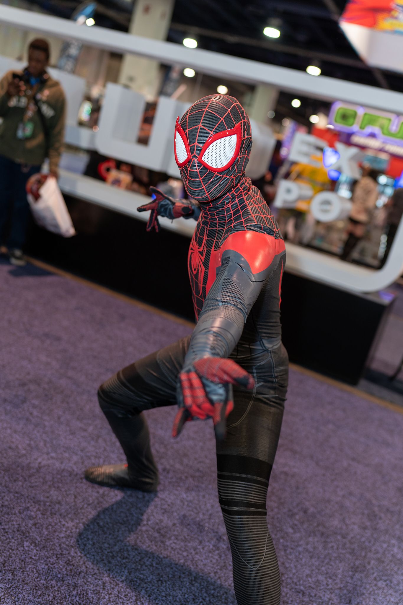 Spider-Man cosplayer in Miles Morales suit striking dynamic poses on convention floor.