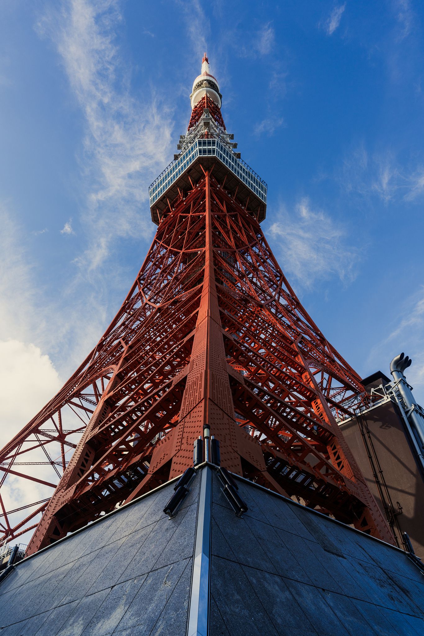 Red and white Tokyo Tower photographed from below against a blue sky.