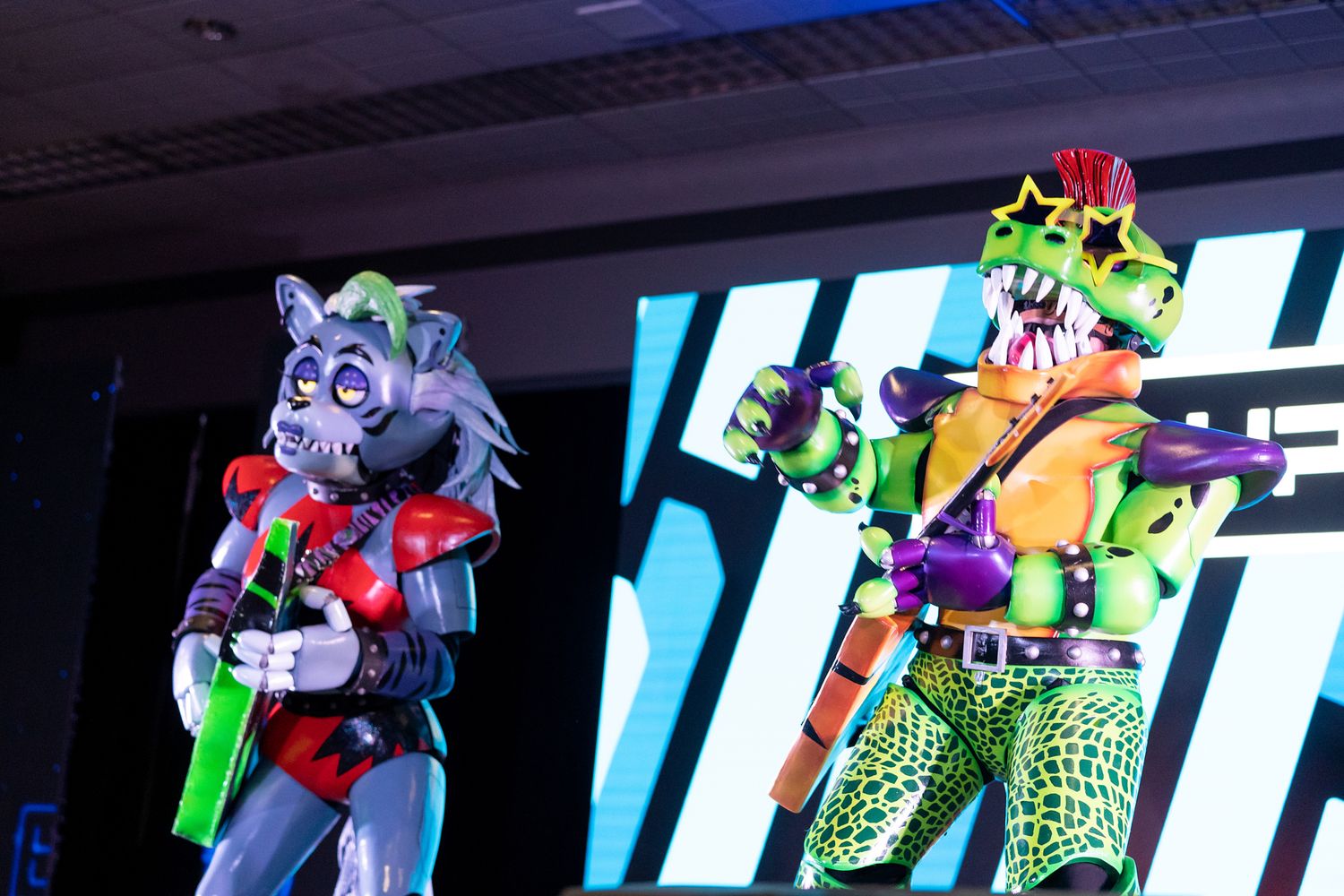 Cosplayers performing on stage with bright LED screen backdrop at convention event.