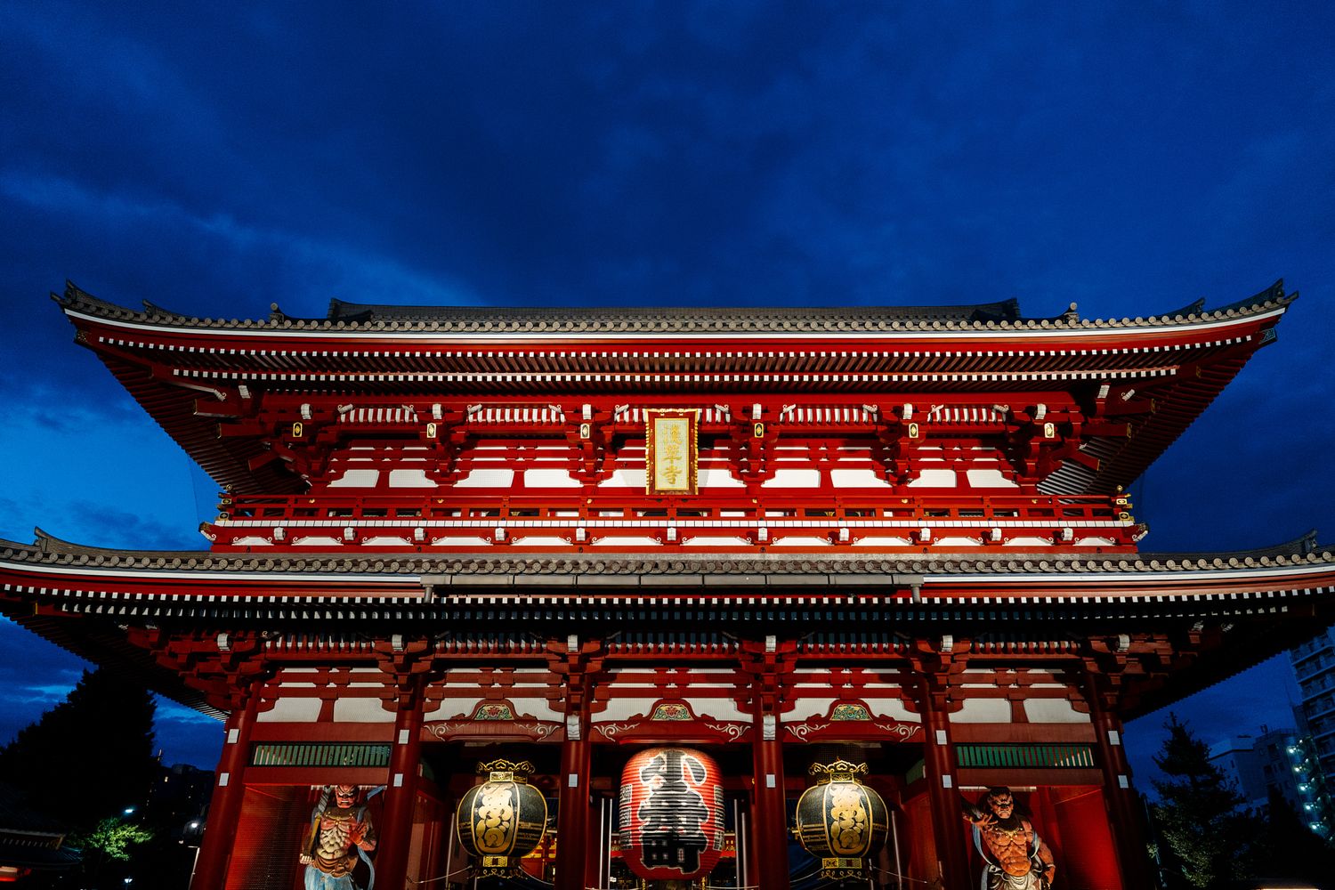 Red and gold Japanese temple architecture stretches across a panoramic view against deep blue sky.