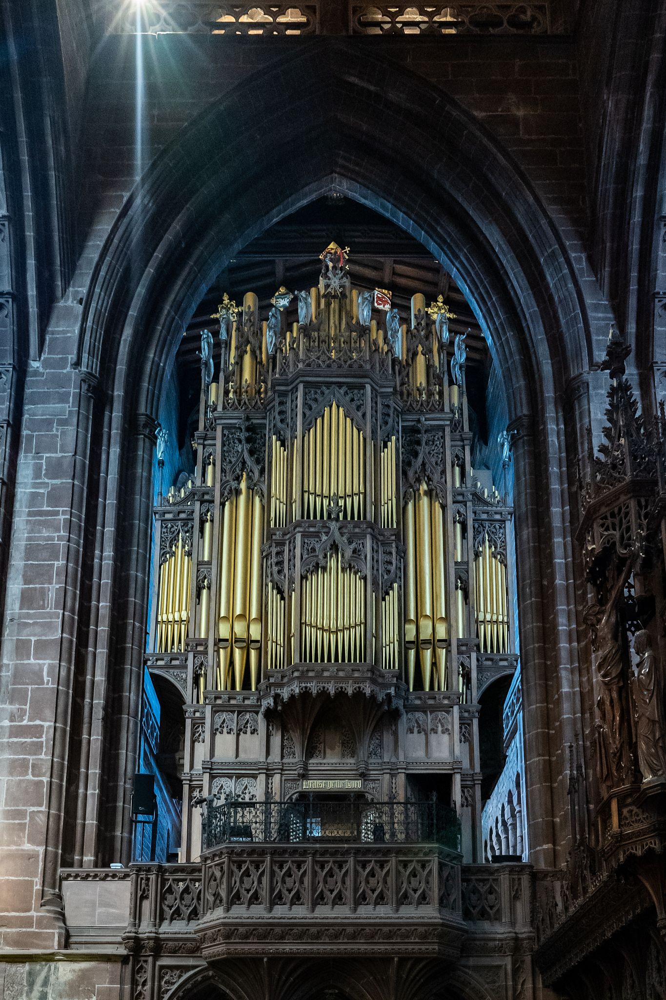 Ornate church pipe organ with golden pipes and gothic architectural details in dramatic lighting.