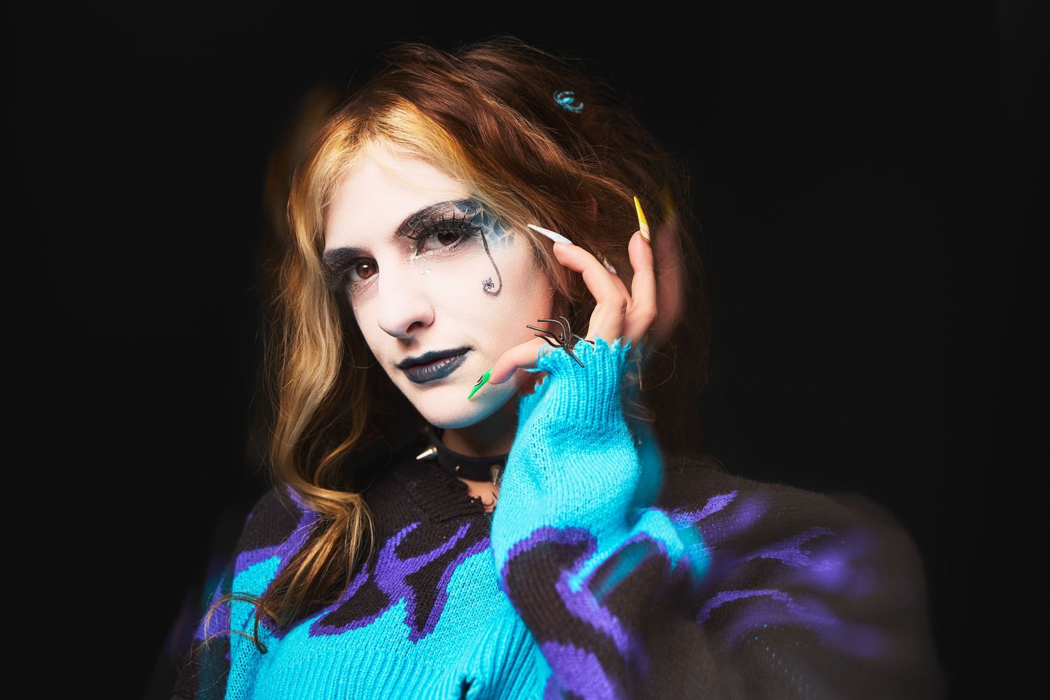 A woman with dramatic dark makeup, blue lips, and colorful body paint poses against a black background.