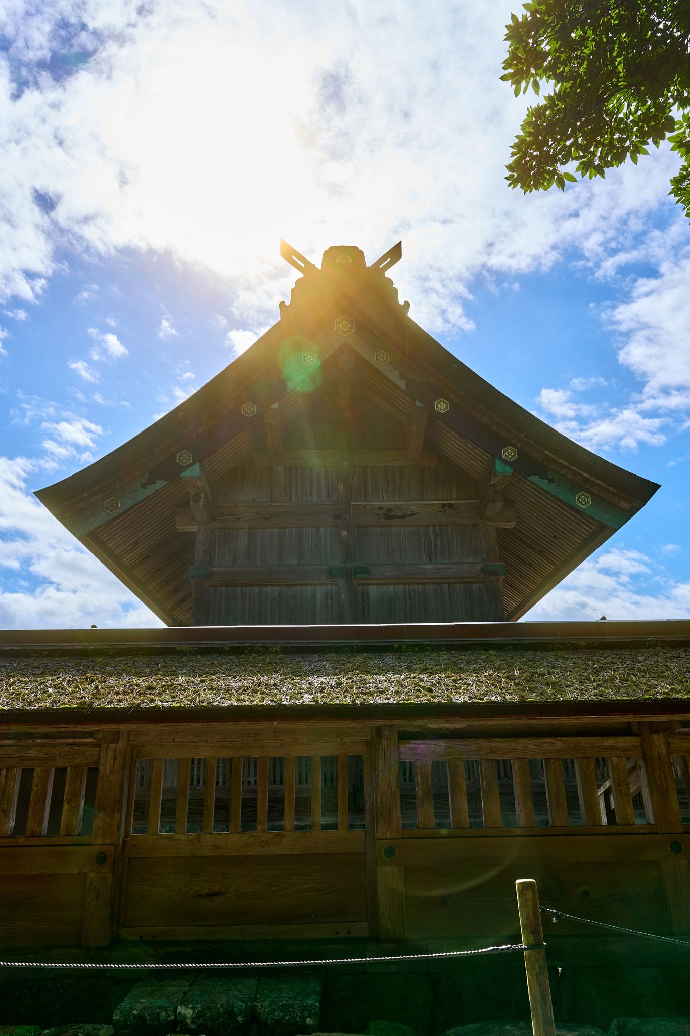 Traditional Japanese temple roof silhouetted against bright sunlit sky.