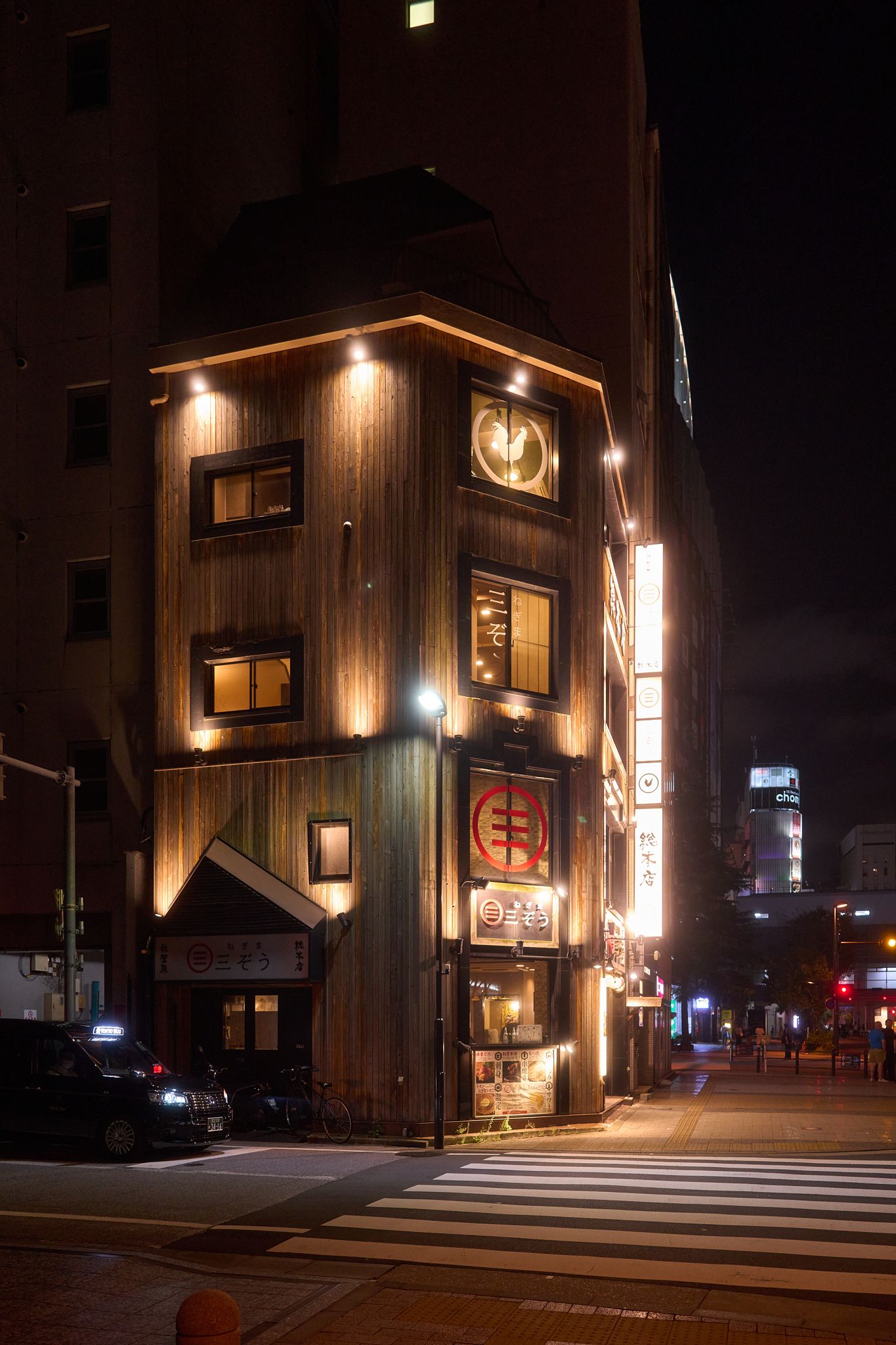 Wooden-clad restaurant exterior illuminated at night with warm lighting and street signage.