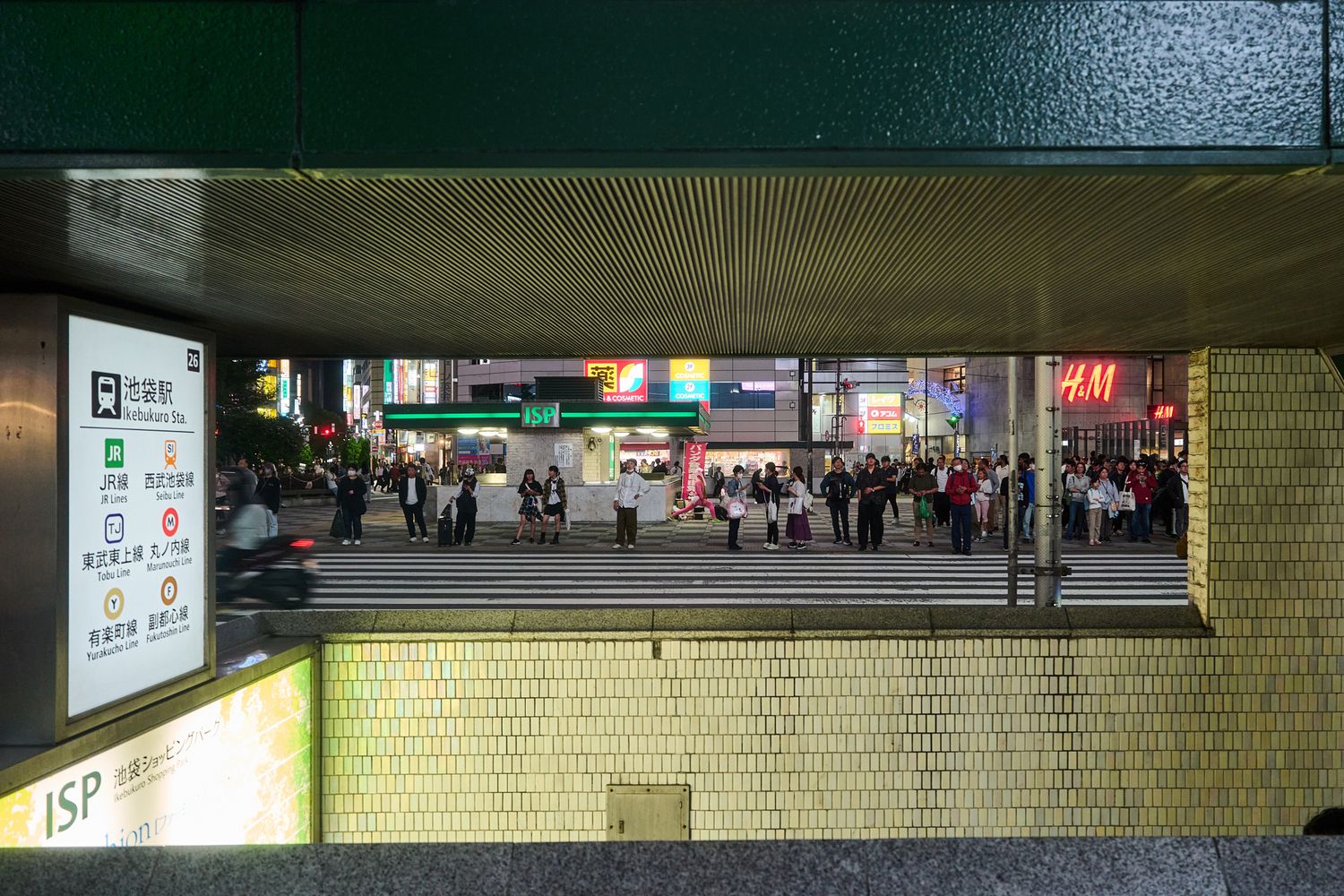 Underground passage with yellow tiled walls and fluorescent lighting leading to city streets.